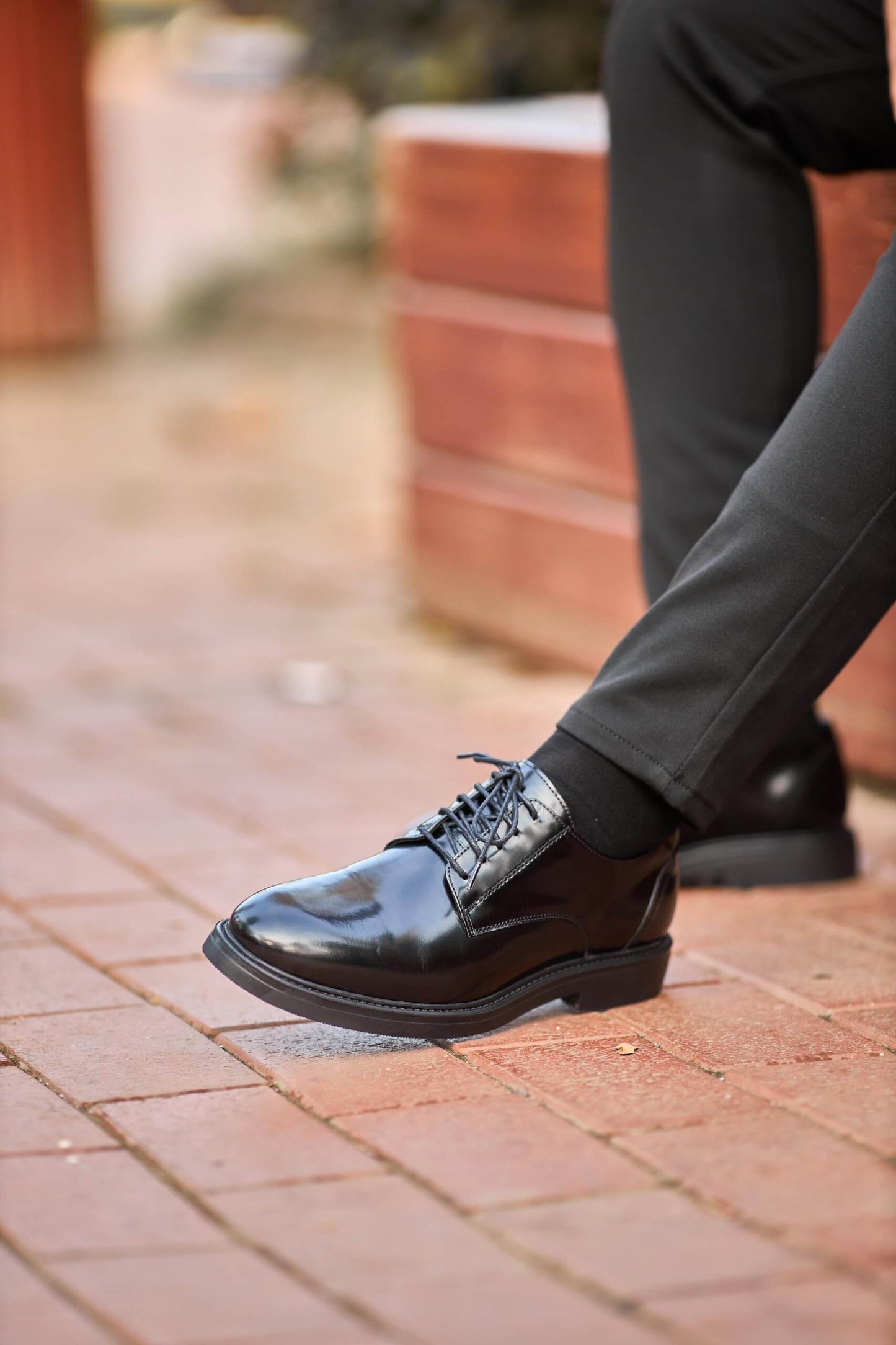 Black polished leather Derby shoes worn with black trousers, styled on outdoor wooden bench.