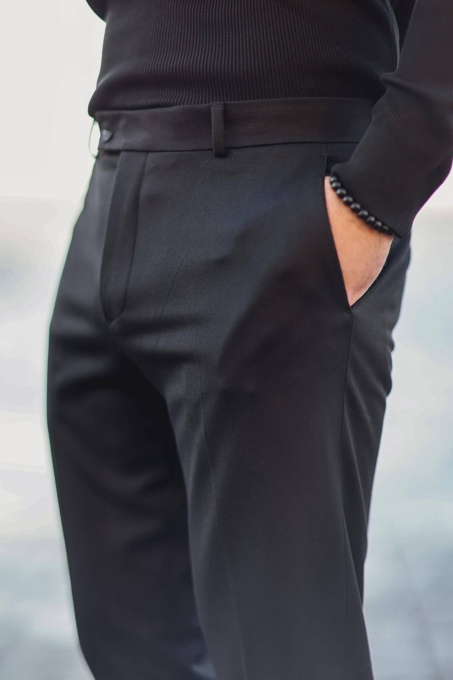 Man wearing black slim-fit tailored trousers with hands in pockets, styled with a black ribbed top.