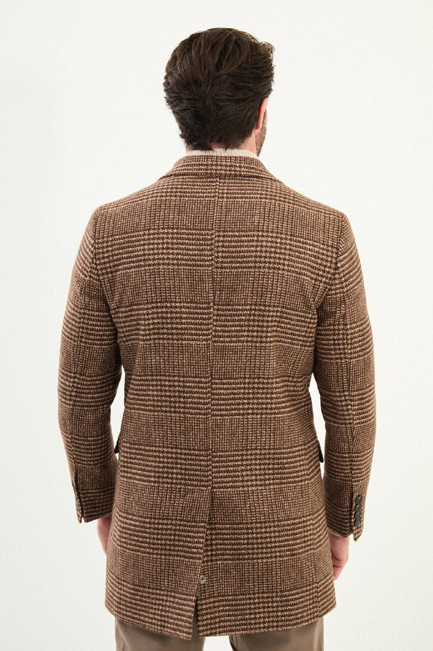 Men’s brown double-breasted herringbone wool-blend longline overcoat with extra-wide peak lapels, deep overlap front, and styled with a cream turtleneck.