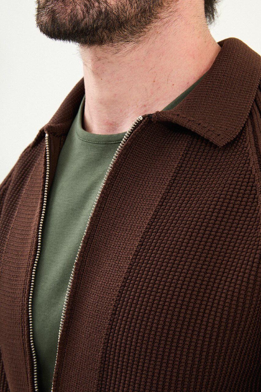 A man wearing a slim fit brown ribbed zip cardigan with a polo collar, styled with beige trousers.
