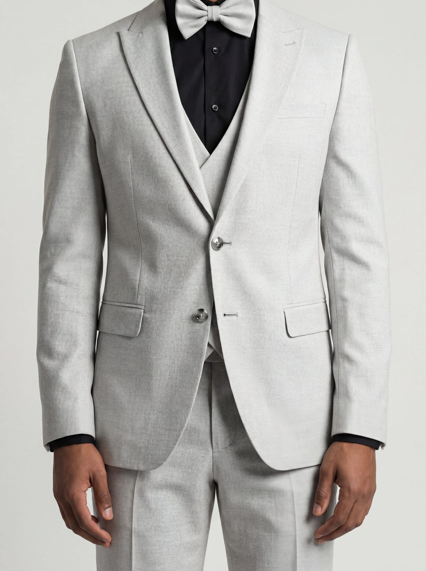 Young man wearing HolloMen's Gray Tuxedo Suit for prom, standing outdoors in a modern setting, featuring a black shirt and a stylish bow tie, showcasing a sleek and sophisticated look.