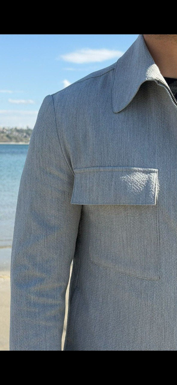 Men’s light grey co-ord set featuring a zip-up jacket with chest pockets and slim-fit trousers, styled in an outdoor waterfront setting.