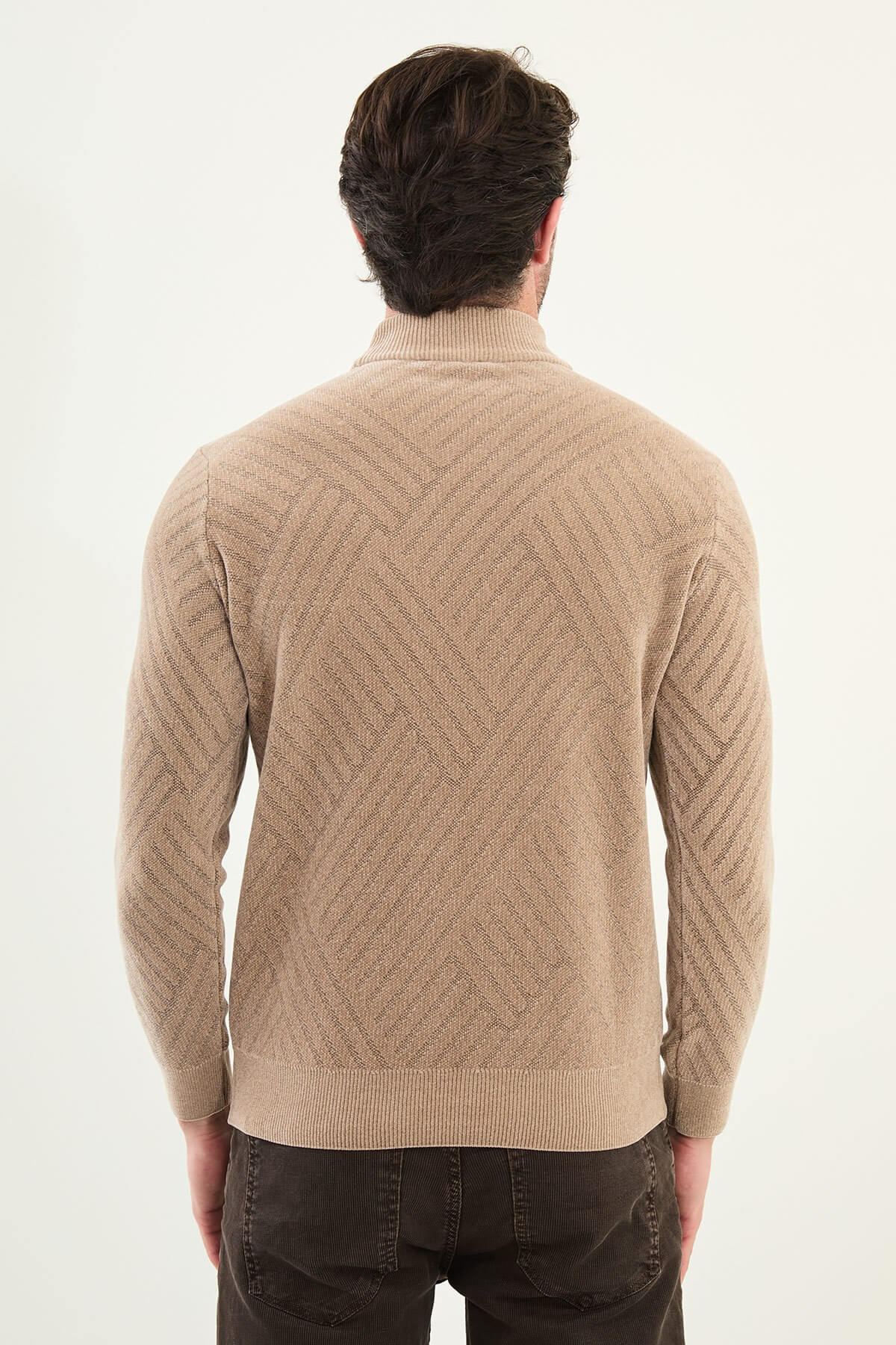 A man wearing a slim fit beige turtleneck knitwear sweater with geometric patterns, paired with dark trousers for a refined fall-winter look.