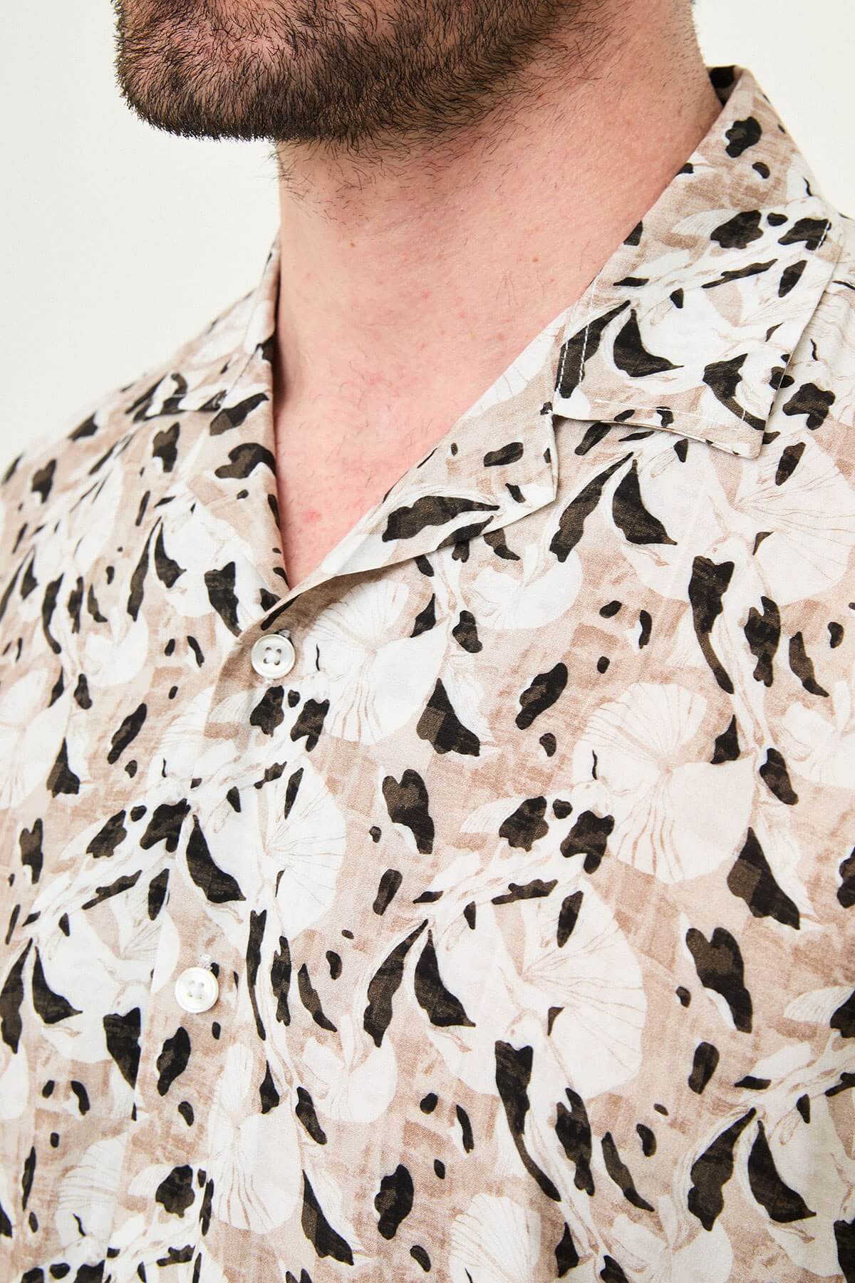 Men wearing a camel-patterned short-sleeved casual shirt, slim fit, standing with one hand in pocket, styled with dark trousers.