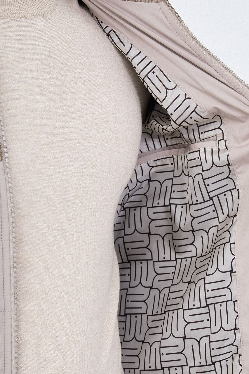 Beige men's casual jacket styled with a cream sweater and dark trousers.