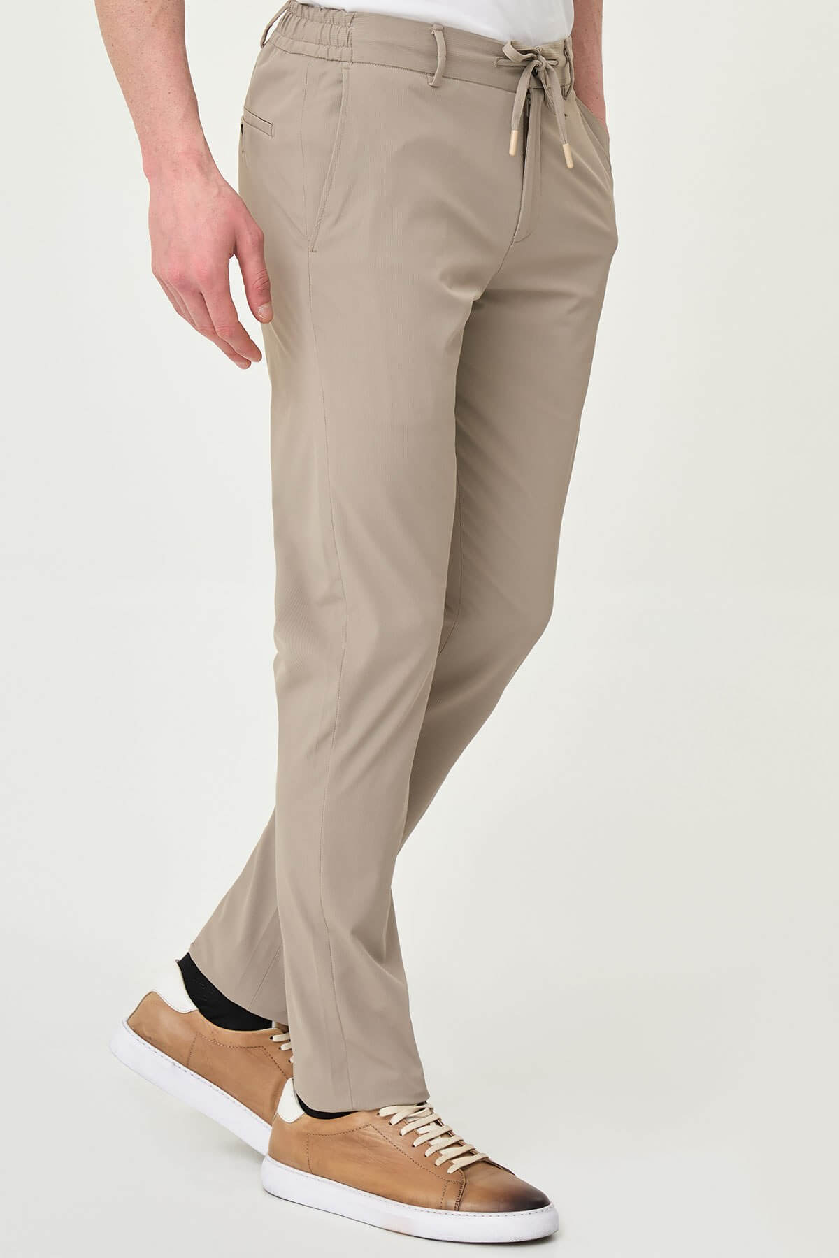 Man wearing beige slim-fit summer trousers styled with white sneakers and a white polo shirt.