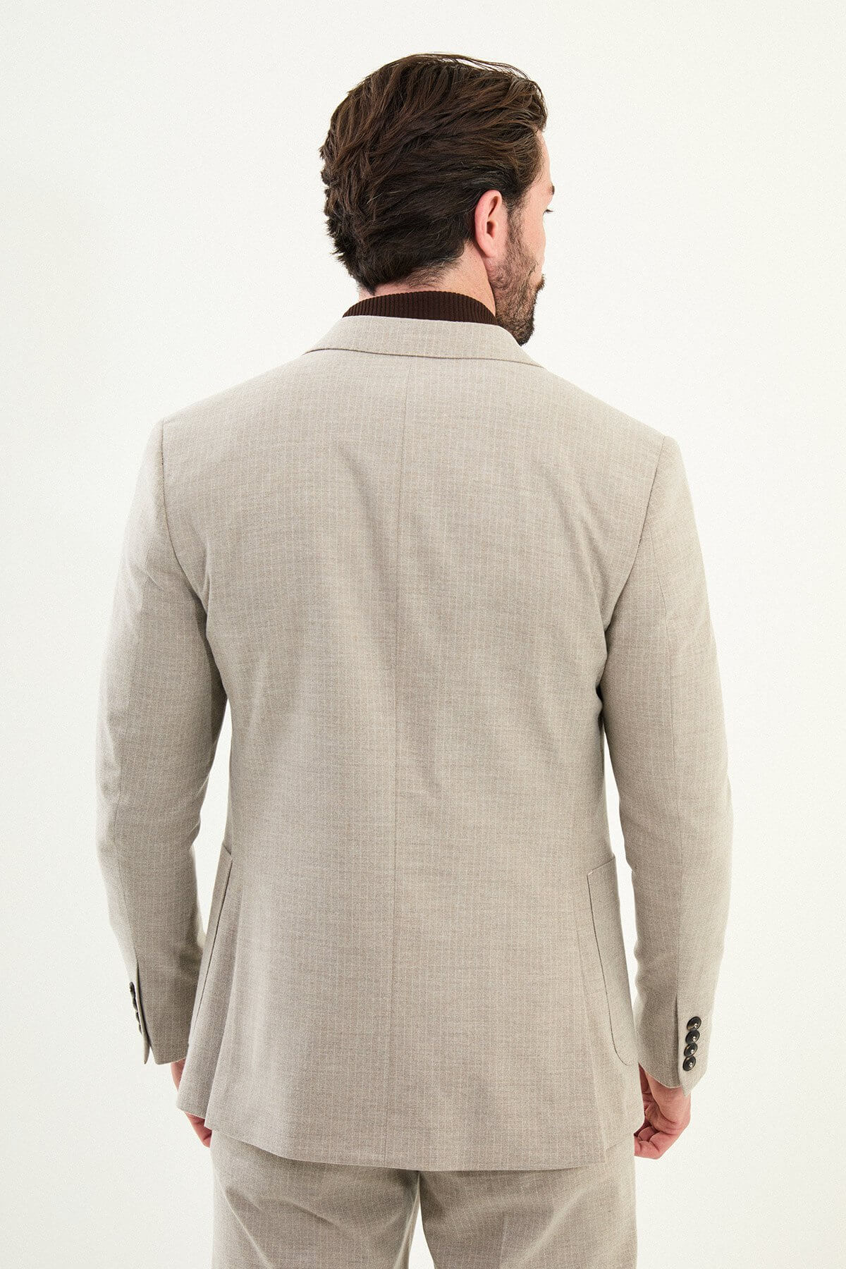 Men’s beige slim-fit mono-collar (mandarin collar) winter suit with minimalist single-breasted jacket, matte micro-texture active-recovery fabric, styled with a dark brown turtleneck.