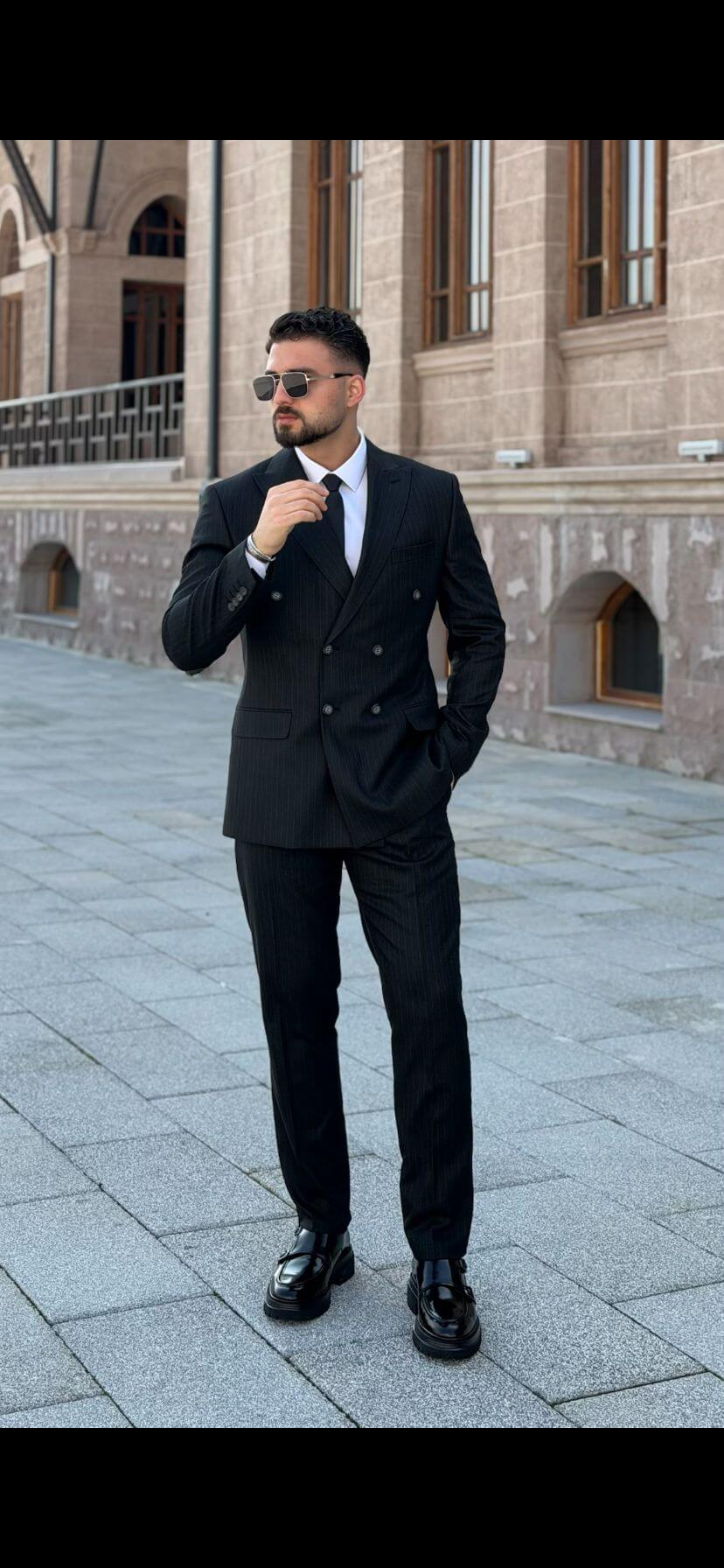 Black double breasted suit with peak lapel, white shirt and black tie, front view