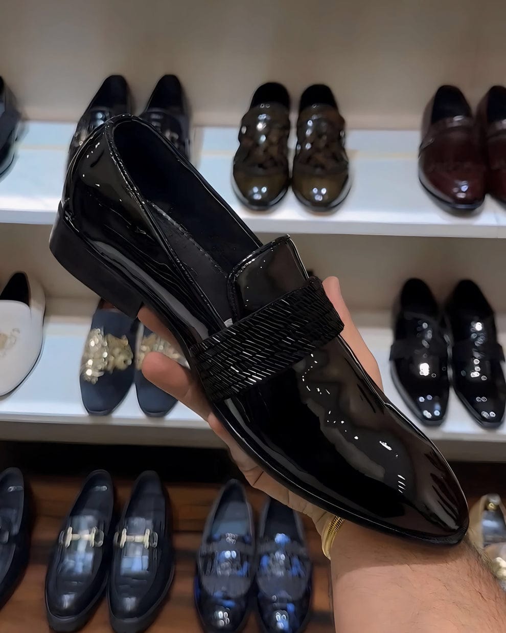 Black patent leather loafers with a glossy finish and woven strap detail, styled for both formal and semi-formal occasions.