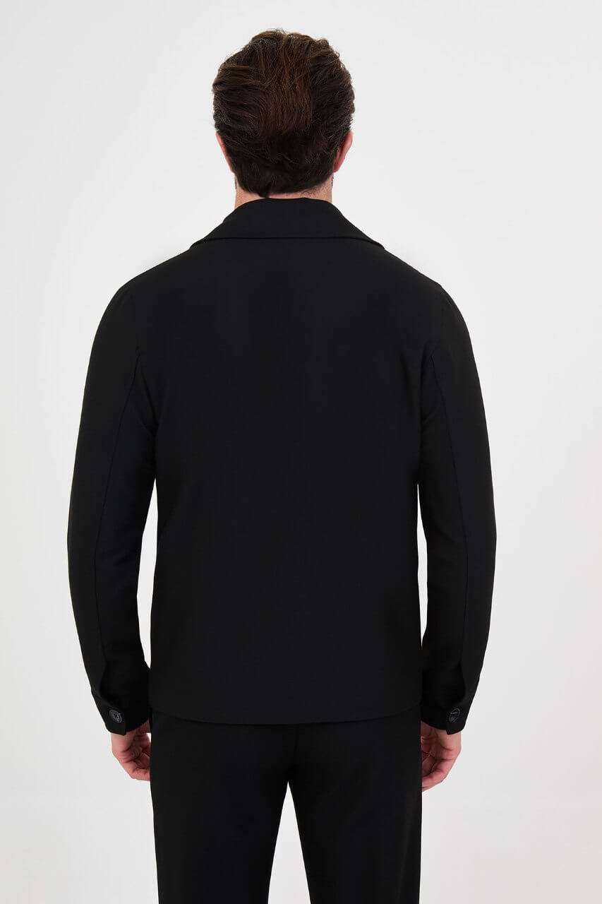 Men's black fall/winter utility jacket styled with a burgundy crew-neck shirt and black trousers.