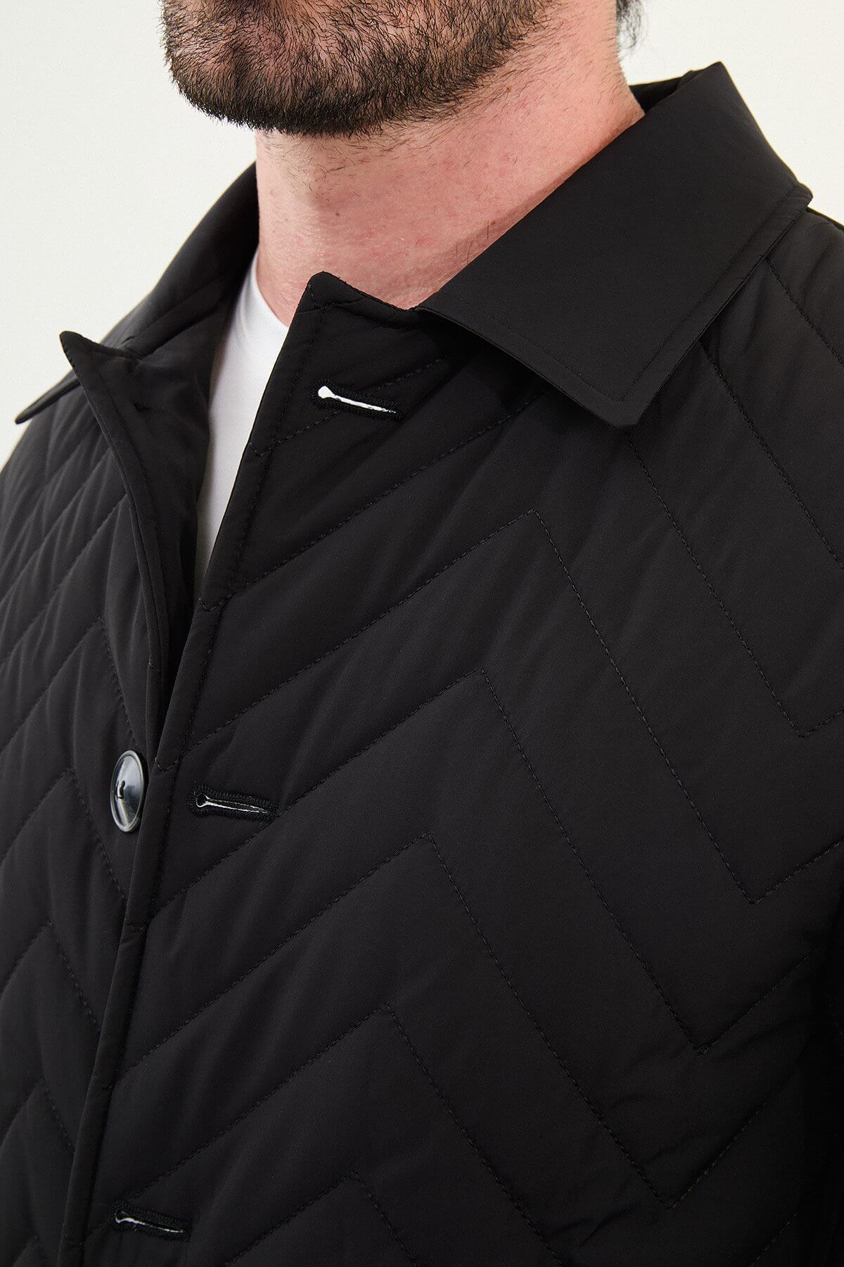 Full-body view of model wearing men's black quilted car coat styled with grey jeans and sneakers.