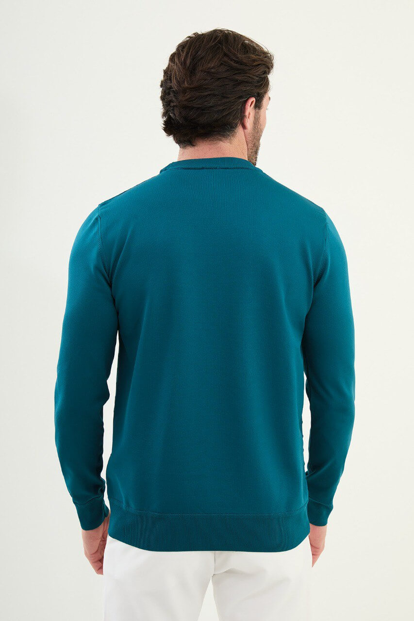 Men’s teal-blue slim-fit crew-neck sweater with geometric ‘T’ textured knit front panel, cotton-viscose-elastane blend, styled with white trousers.