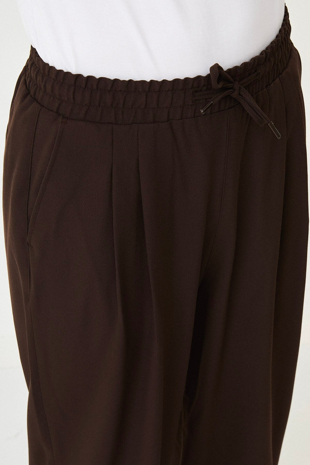 Men wearing brown luxe drawstring jersey pants with white sneakers, styled for a smart-casual summer look.