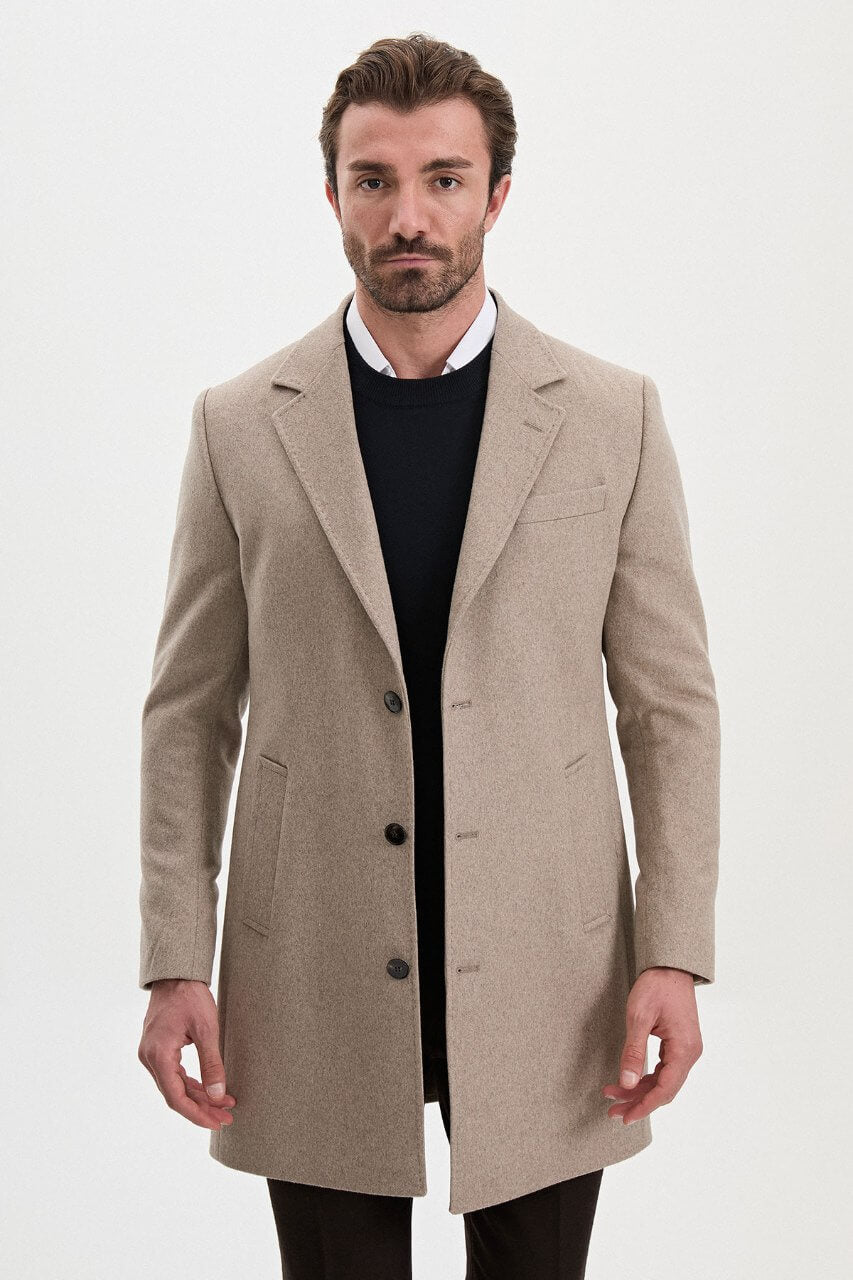 Men's beige single-breasted winter coat styled with a black sweater, dark trousers, and brown leather boots.