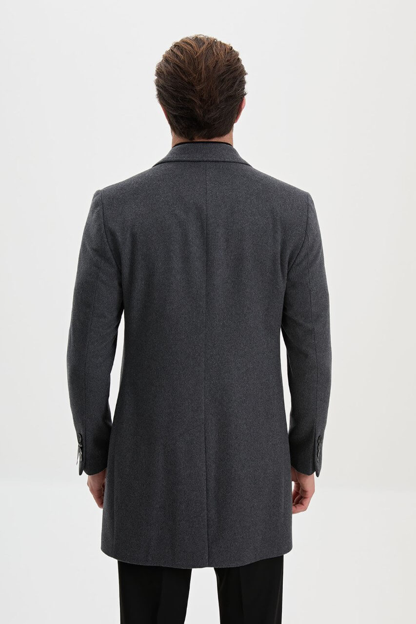 Men's dark grey single-breasted winter overcoat styled with a black roll-neck sweater and tailored trousers.
