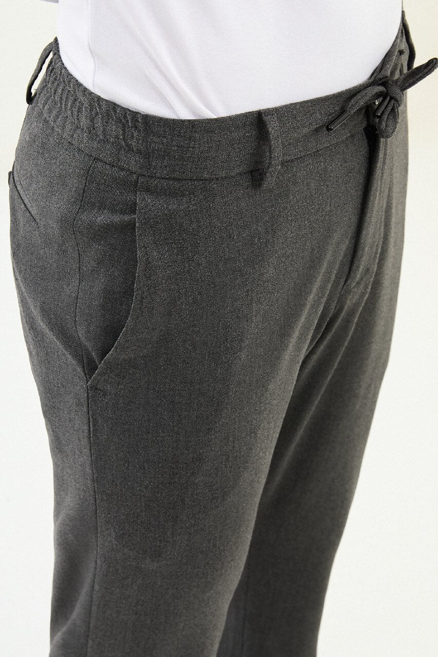 Men wearing dark gray slim-fit drawstring trousers with elastic waistband, casual-formal hybrid, styled with sneakers and dress shoes for versatile summer menswear.