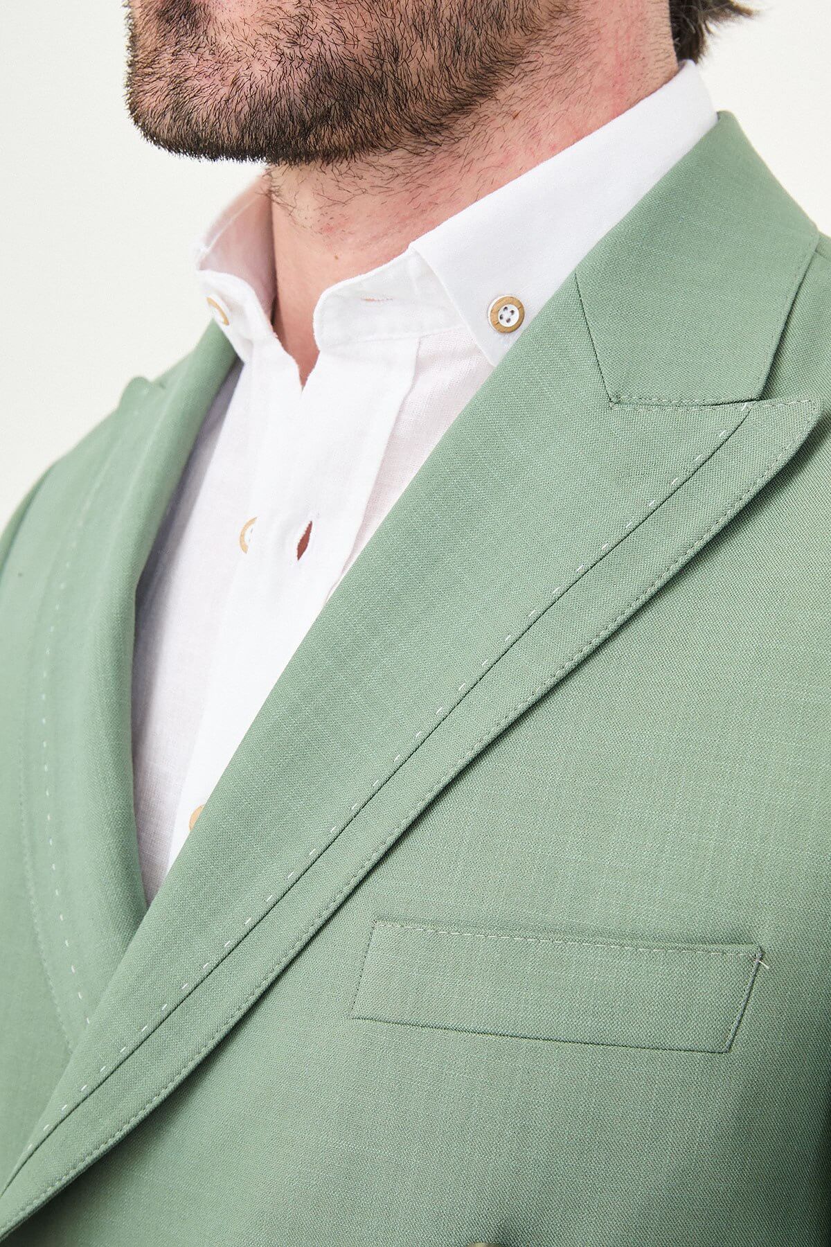 a green slim-fit double-breasted linen-blend suit with peak lapels, matching trousers, an open-collar white shirt, and white leather sneakers.