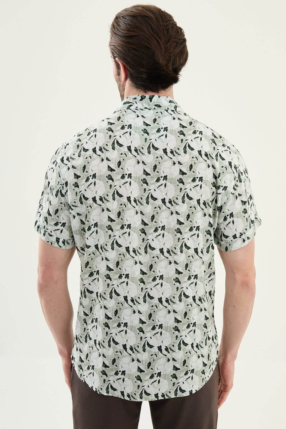 Men wearing a green patterned short-sleeve summer shirt with tropical floral and leaf print, styled casually with light summer trousers.