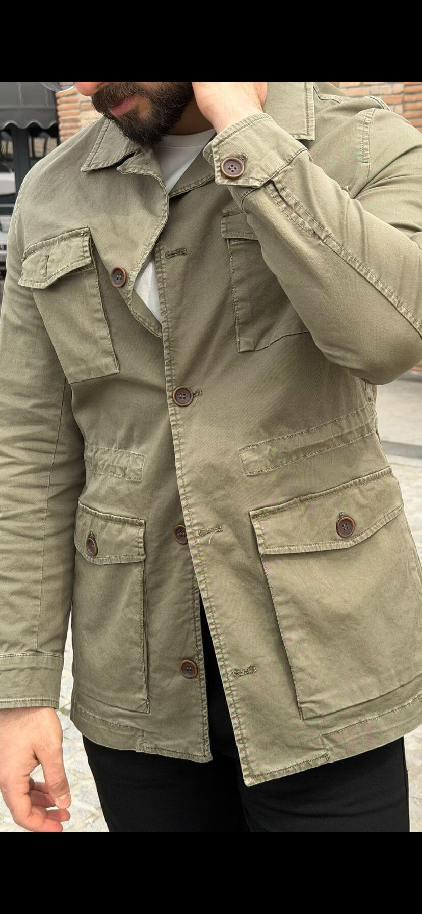 Men’s khaki field jacket with multiple front pockets, worn casually with a white t-shirt and black pants in an outdoor setting.