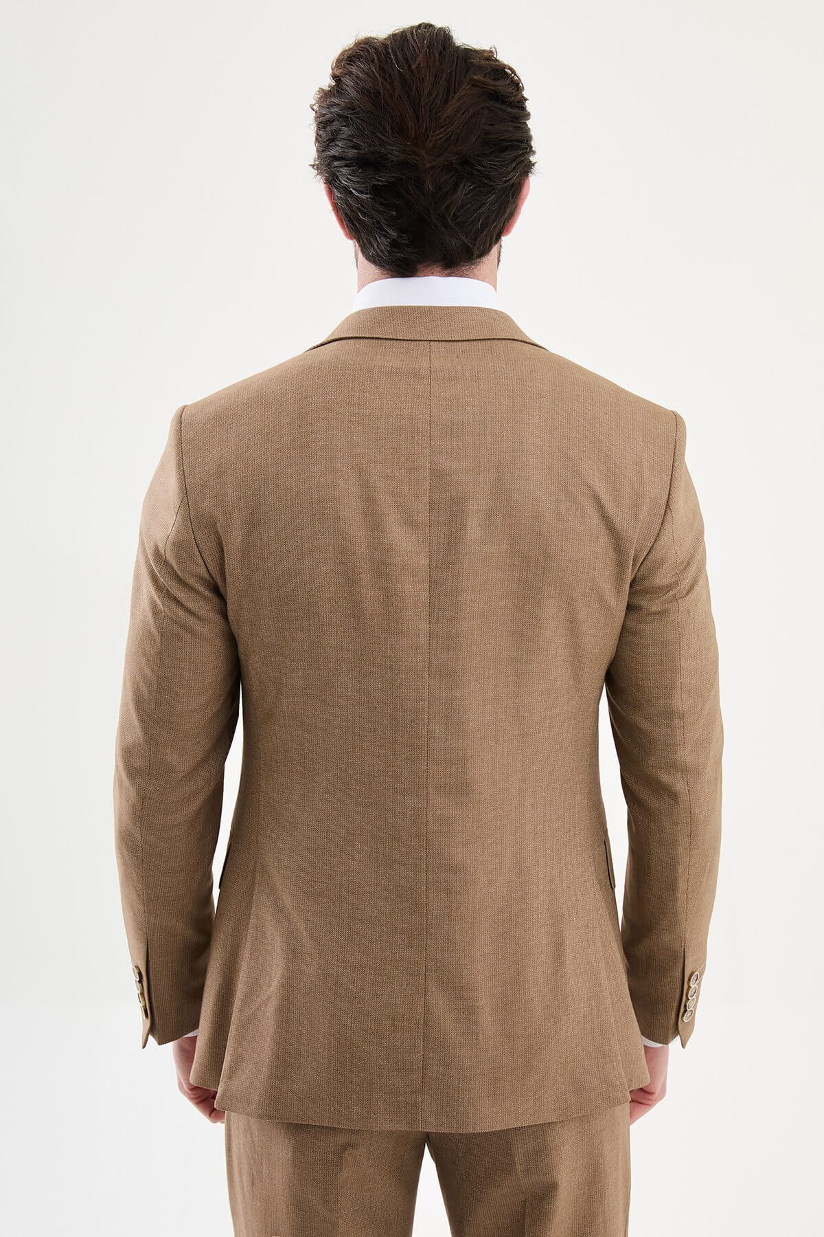 Model wearing a camel slim-fit three-piece suit with a white dress shirt, brown patterned tie, matching waistcoat, tailored trousers, and dark brown leather Derby shoes.