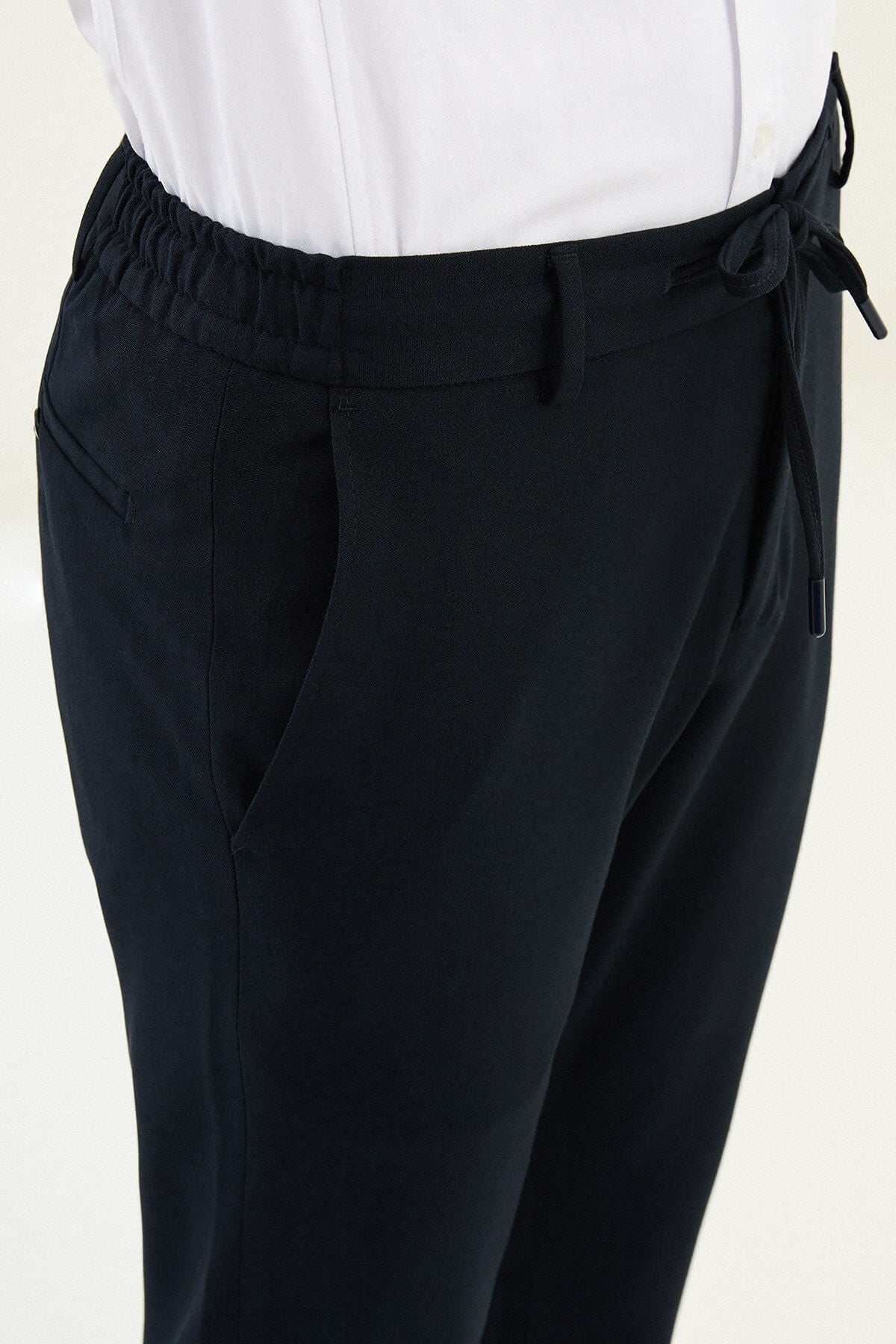 Men wearing navy blue slim-fit drawstring trousers with elastic waistband, tapered slim fit, styled with dress shoes and sneakers for versatile summer menswear.