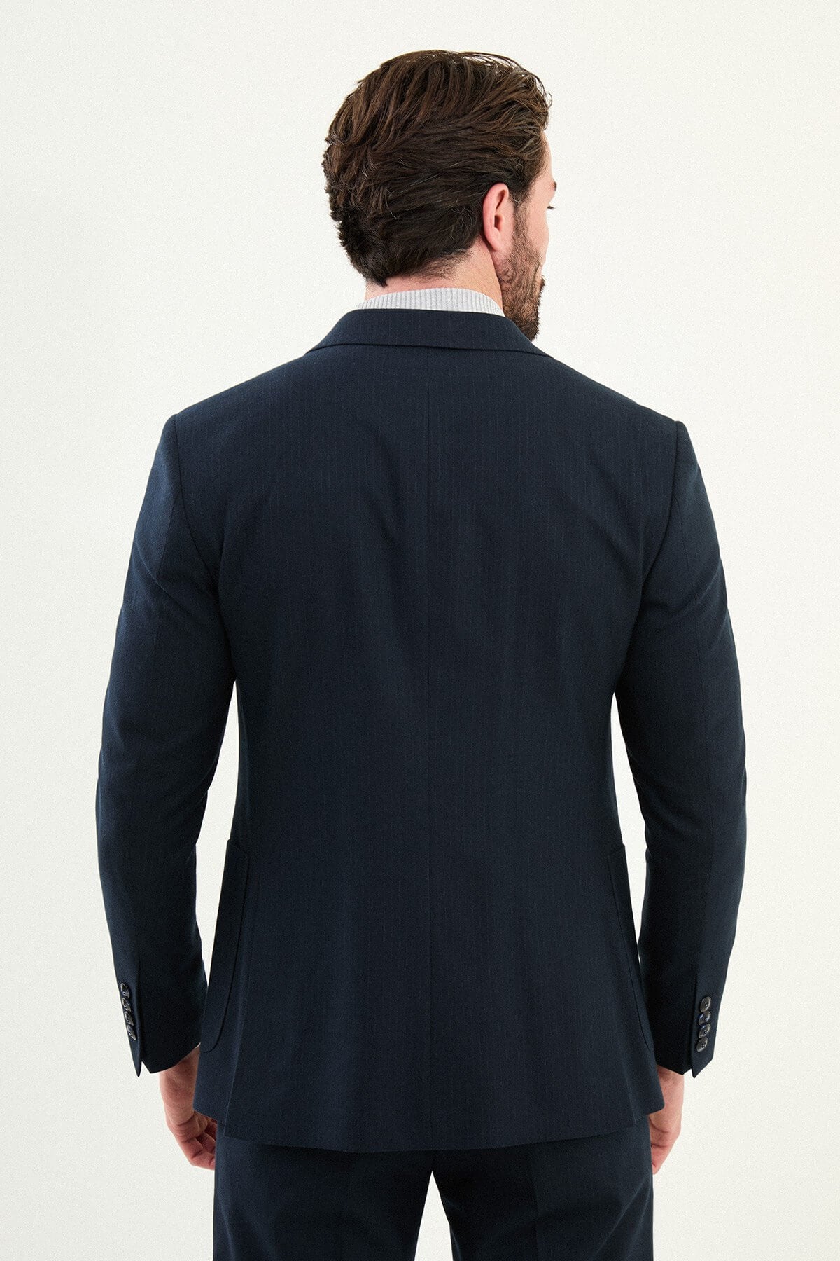 Men’s navy blue slim-fit suit with notch lapels and two-button jacket, matte micro-textured fabric, styled with a light gray mock-neck sweater for modern winter business wear.