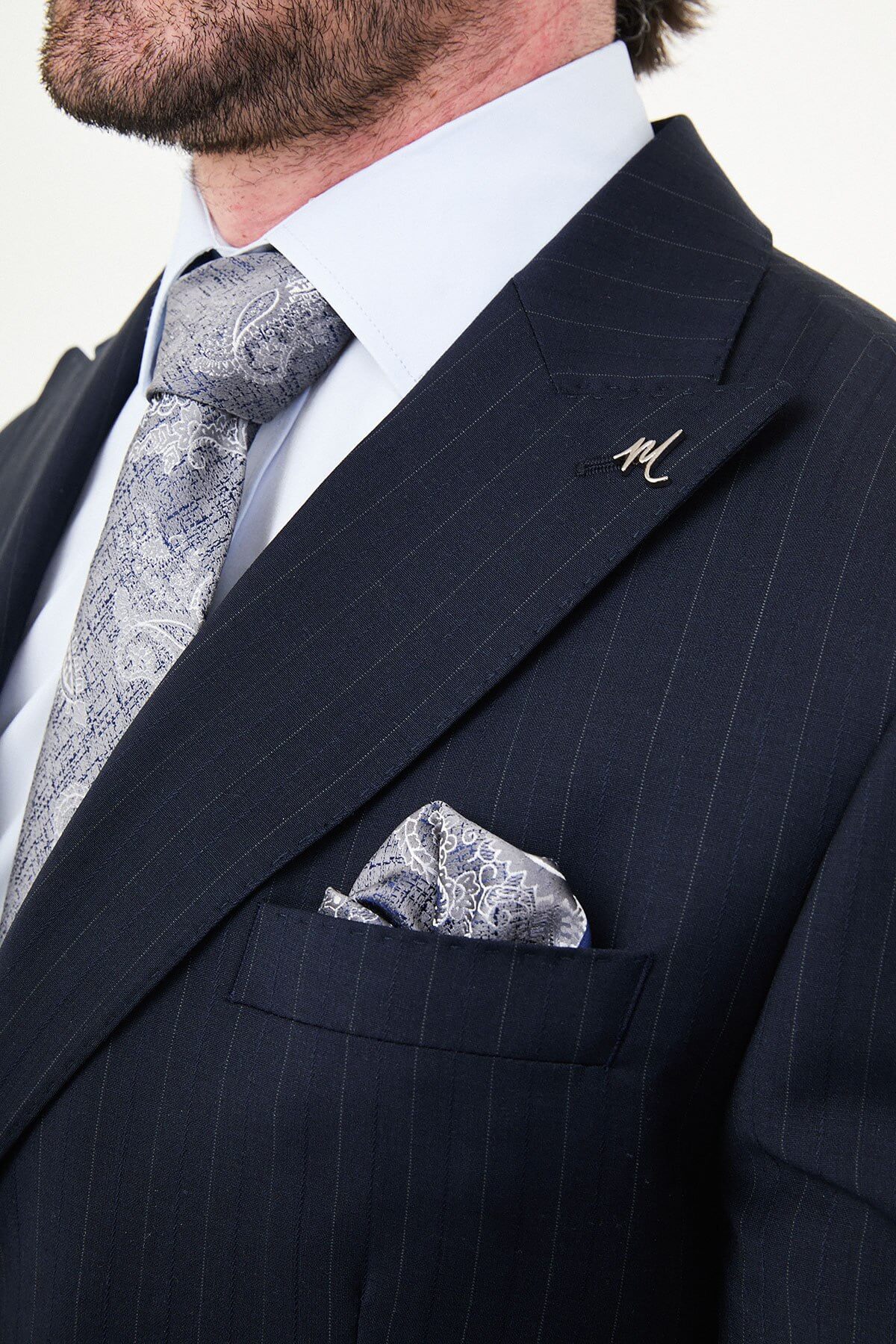 Man wearing a navy blue slim fit premium wool suit with wide collar, styled with matching trousers and a patterned tie
