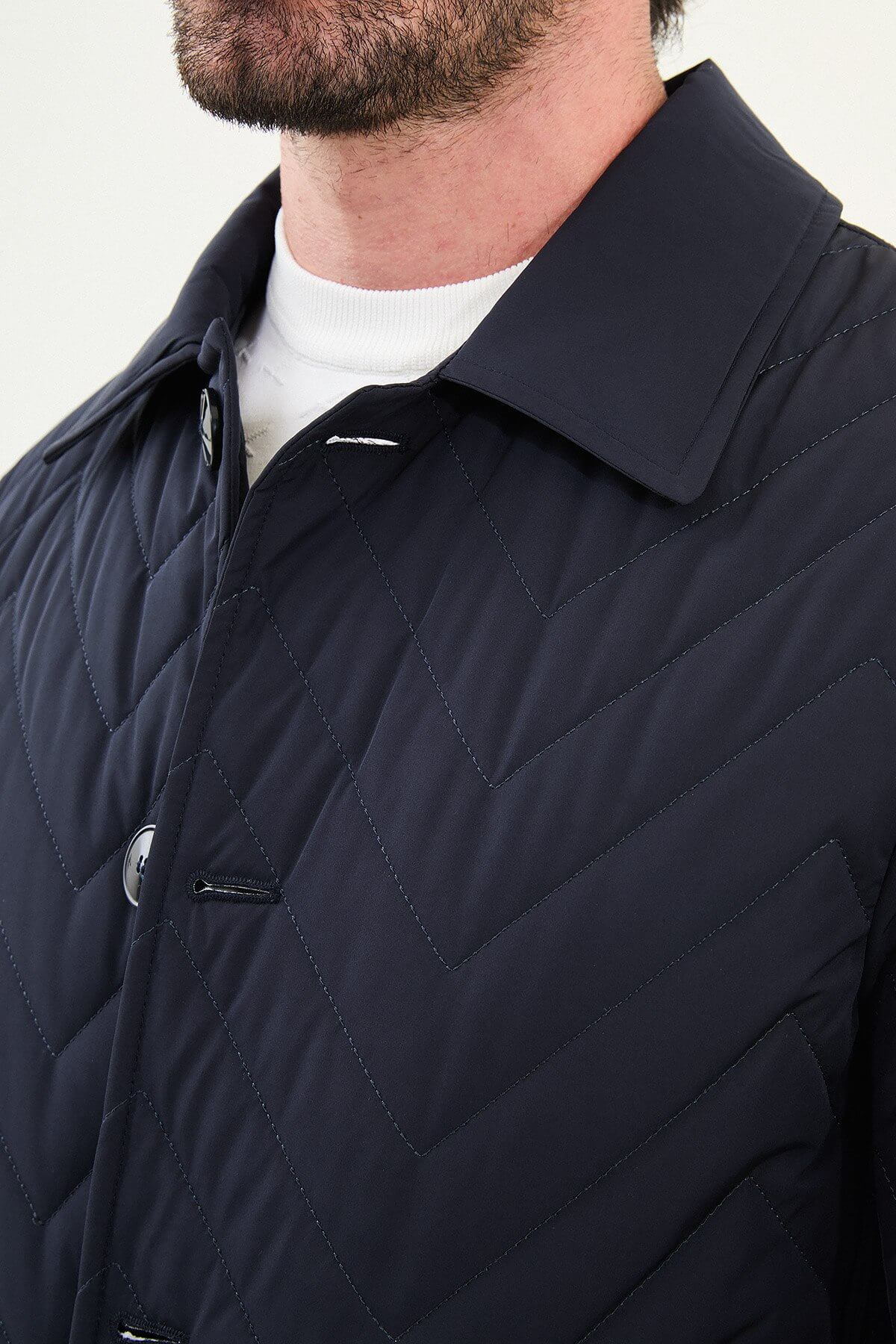Man wearing a navy blue slim fit quilted car coat with button closure, styled with blue jeans and white sneakers.