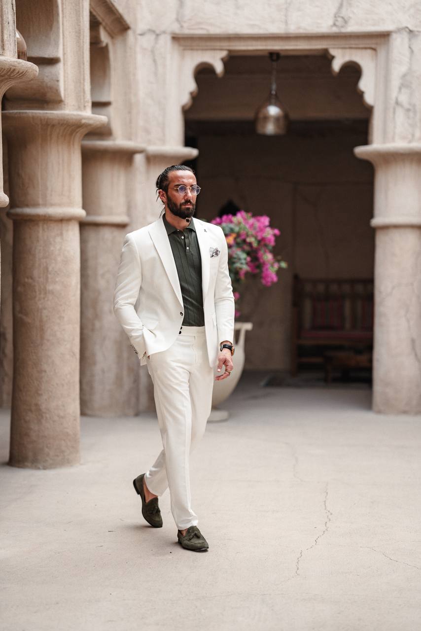 Man styled in HolloMen Monaco White Mono-Collar Summer Suit, paired with an olive-green shirt and loafers, standing elegantly in a Mediterranean-inspired setting.