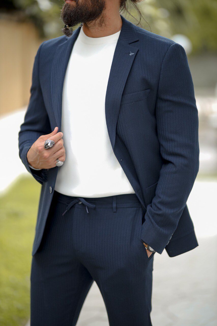 Man wearing a navy blue slim fit seersucker sports suit with a white crewneck top, styled with white sneakers in an outdoor setting.