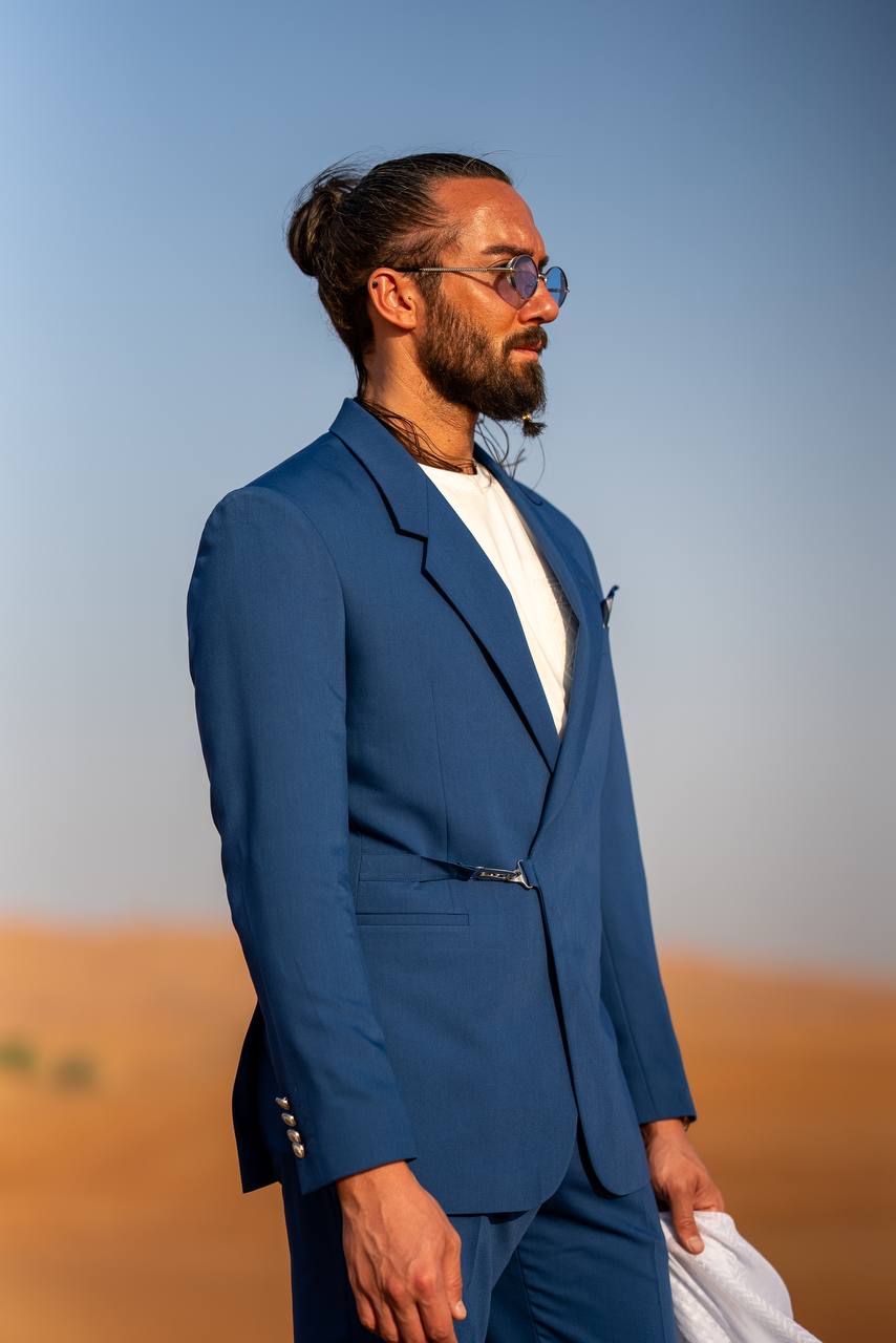 Man wearing HolloMen Amalfi Coast Sax Blue Modern Tailored Suit in a desert setting holding a flowing white scarf.