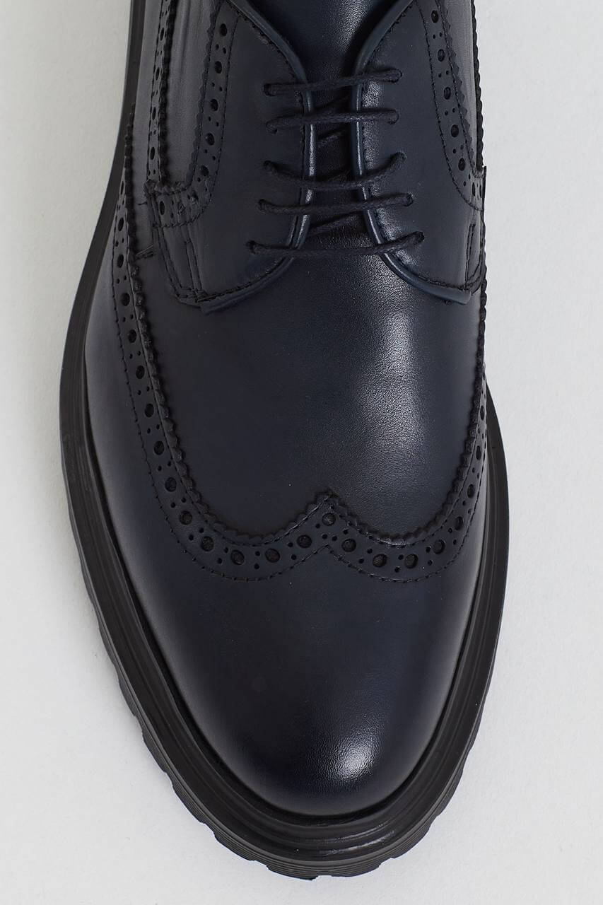 Navy blue leather brogue shoe with intricate perforation details, featuring a chunky black sole, displayed against a minimalist light background.