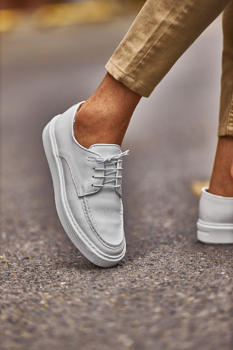 White leather lace-up casual derby shoes worn with beige chinos, photographed outdoors on a city street.