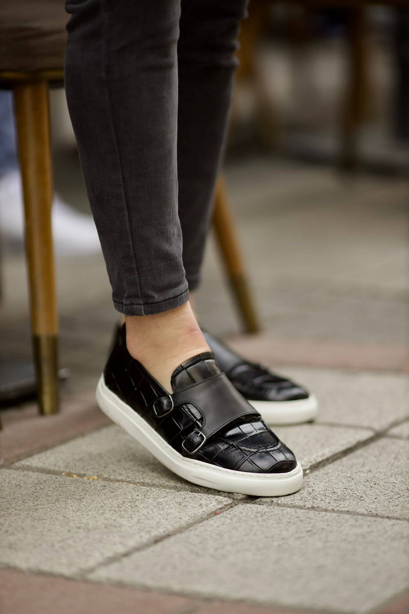 Black crocodile-embossed leather monk loafers with white EVA soles, styled with charcoal pants.