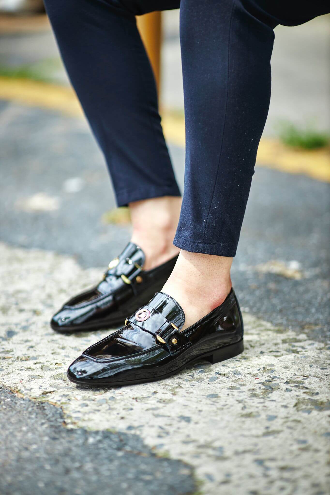 Black patent leather loafers with gold hardware, worn with tailored navy trousers.