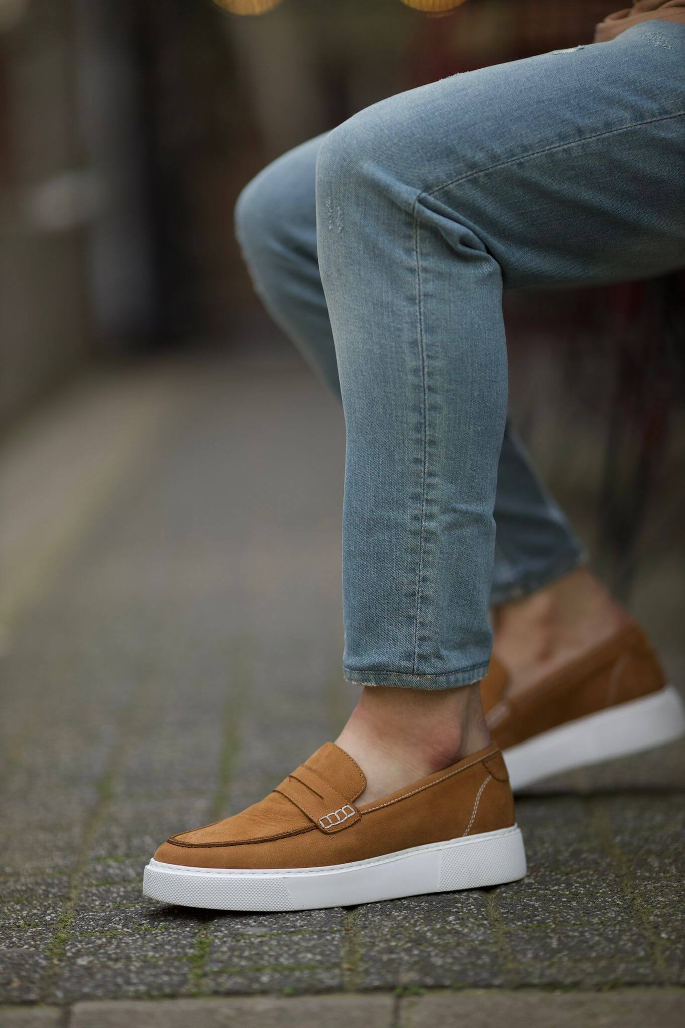 Camel nubuck loafers with white sole, styled with light denim on stone pavement.