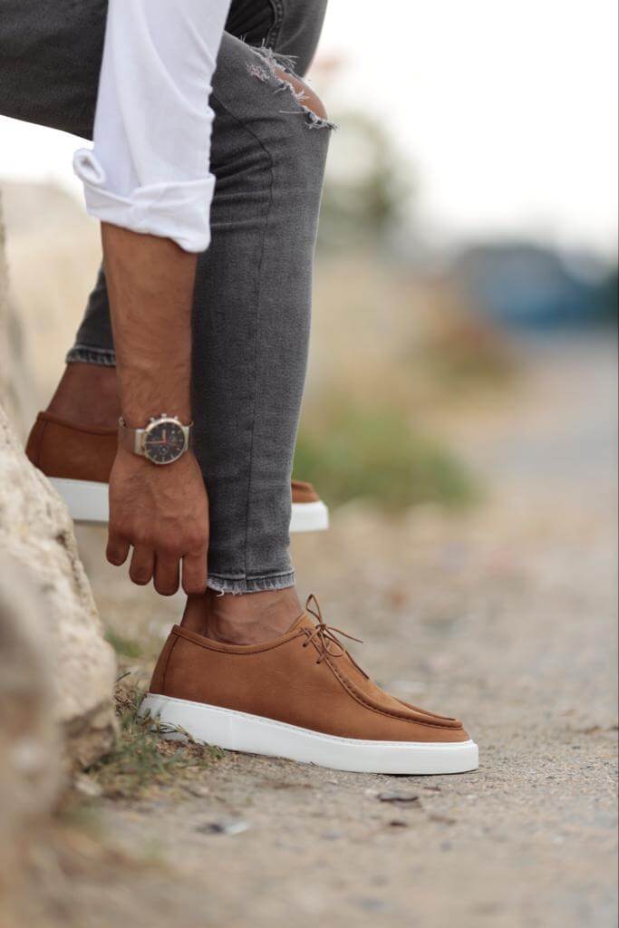 camel suede casual derby shoes with white EVA soles, worn with grey ripped skinny jeans, styled in an outdoor setting against a rusted barrel.