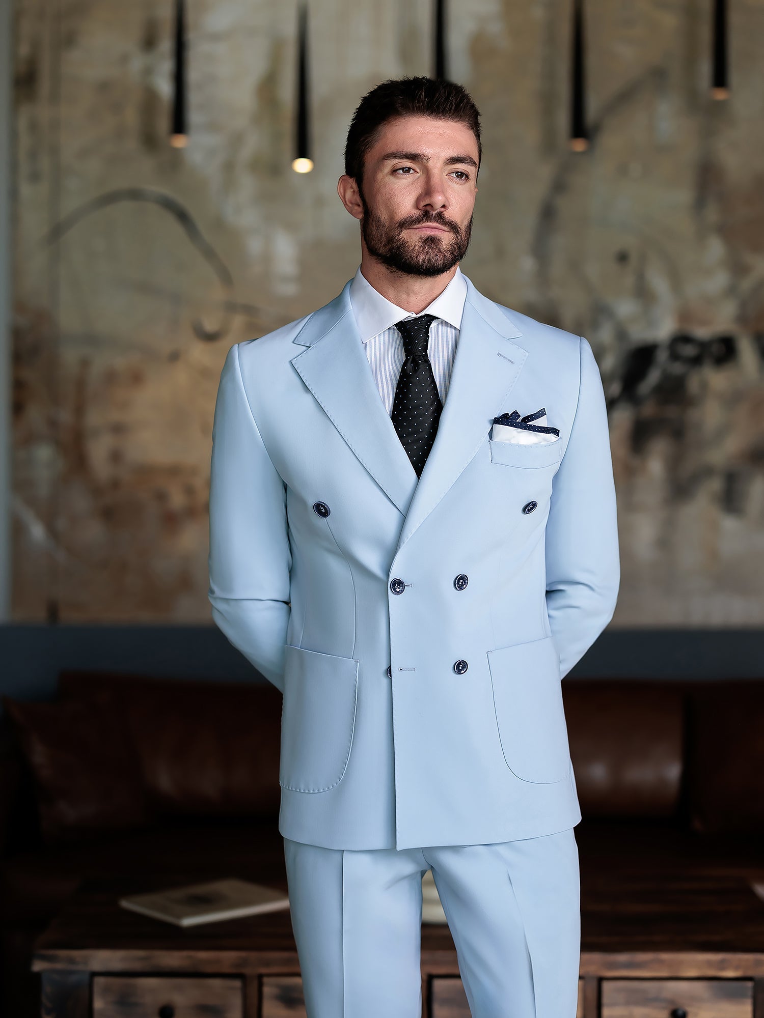 Men wearing a sky-blue double-breasted slim-fit suit with a white shirt and black tie, styled in a modern indoor setting.