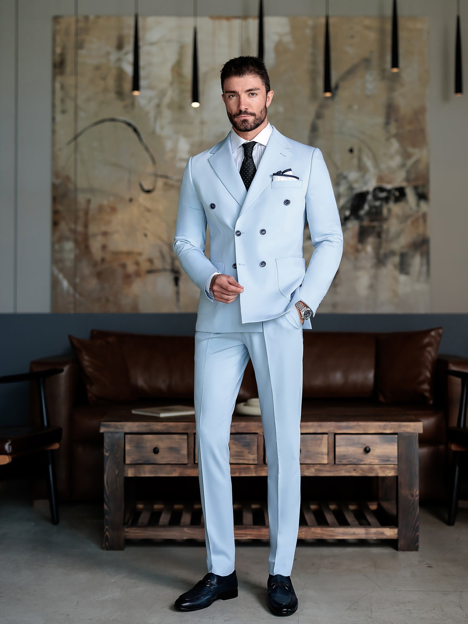 Men wearing a sky-blue double-breasted slim-fit suit with a white shirt and black tie, styled in a modern indoor setting.