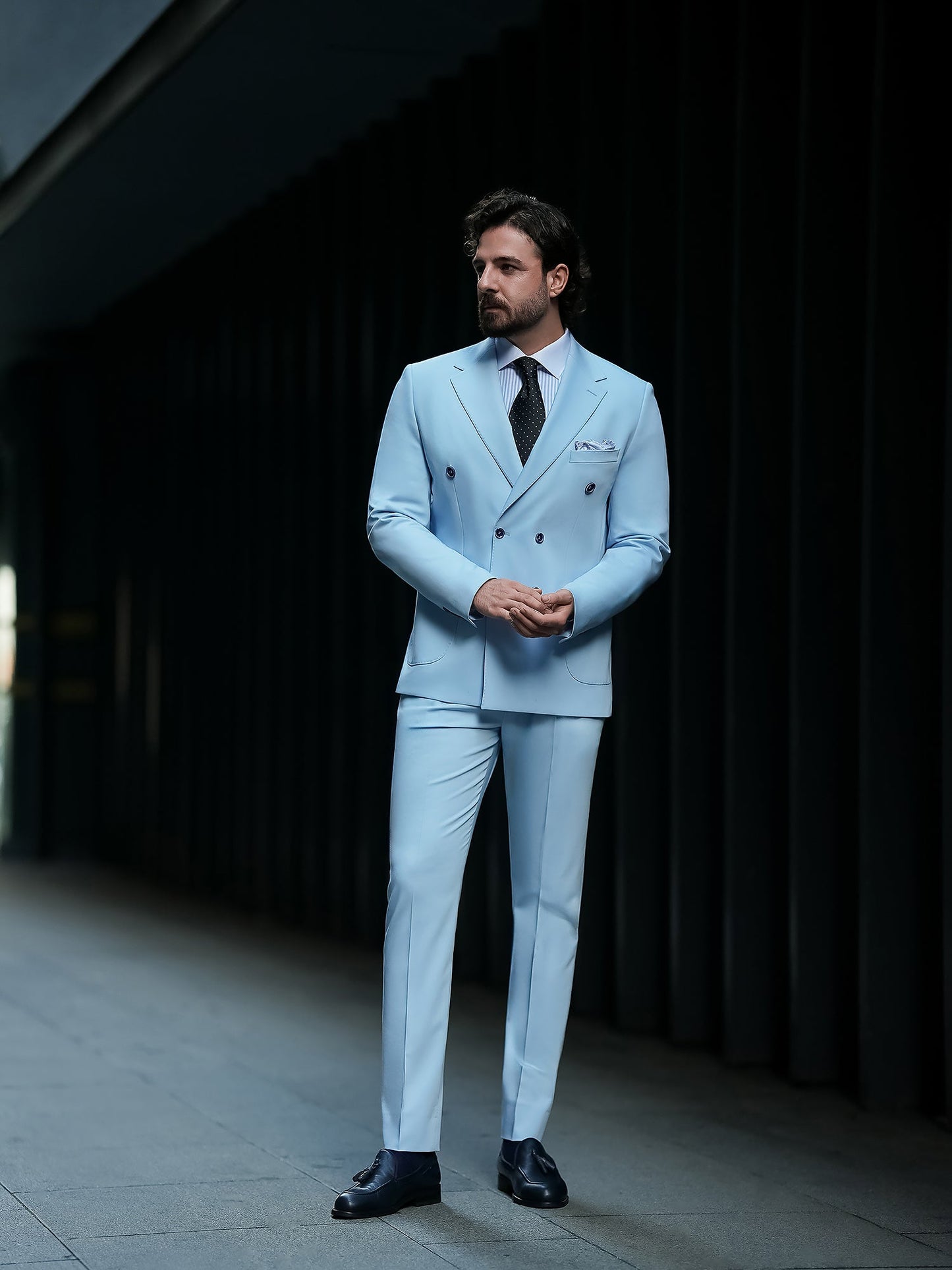 Men wearing a sky-blue double-breasted slim-fit suit with a white shirt and black tie, styled in a modern indoor setting.