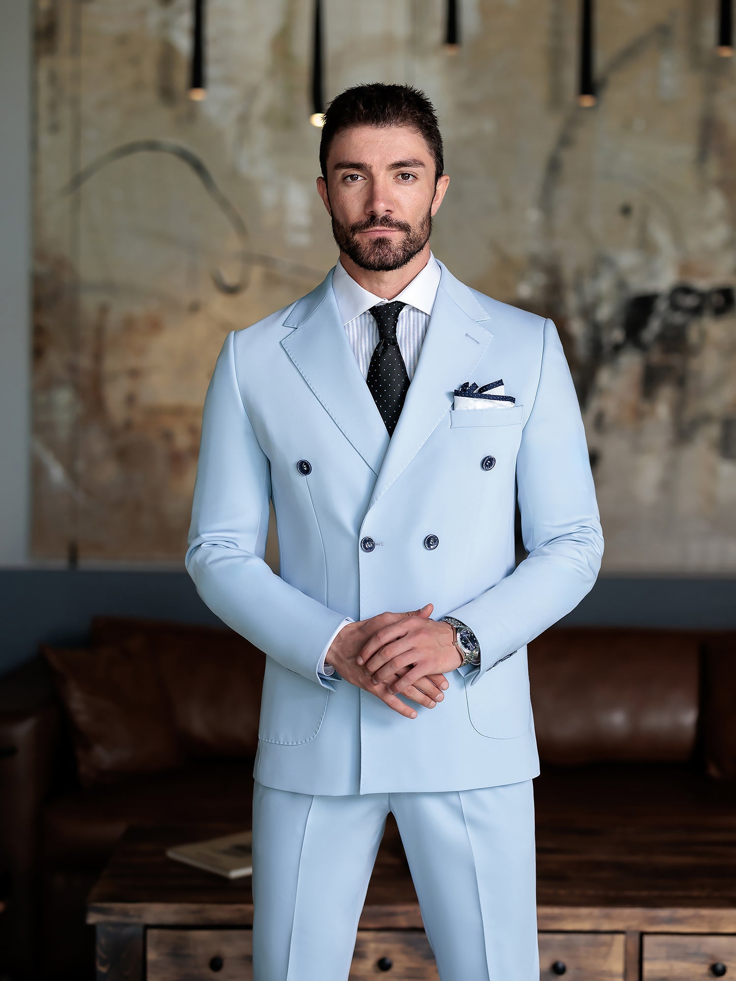 Men wearing a sky-blue double-breasted slim-fit suit with a white shirt and black tie, styled in a modern indoor setting.