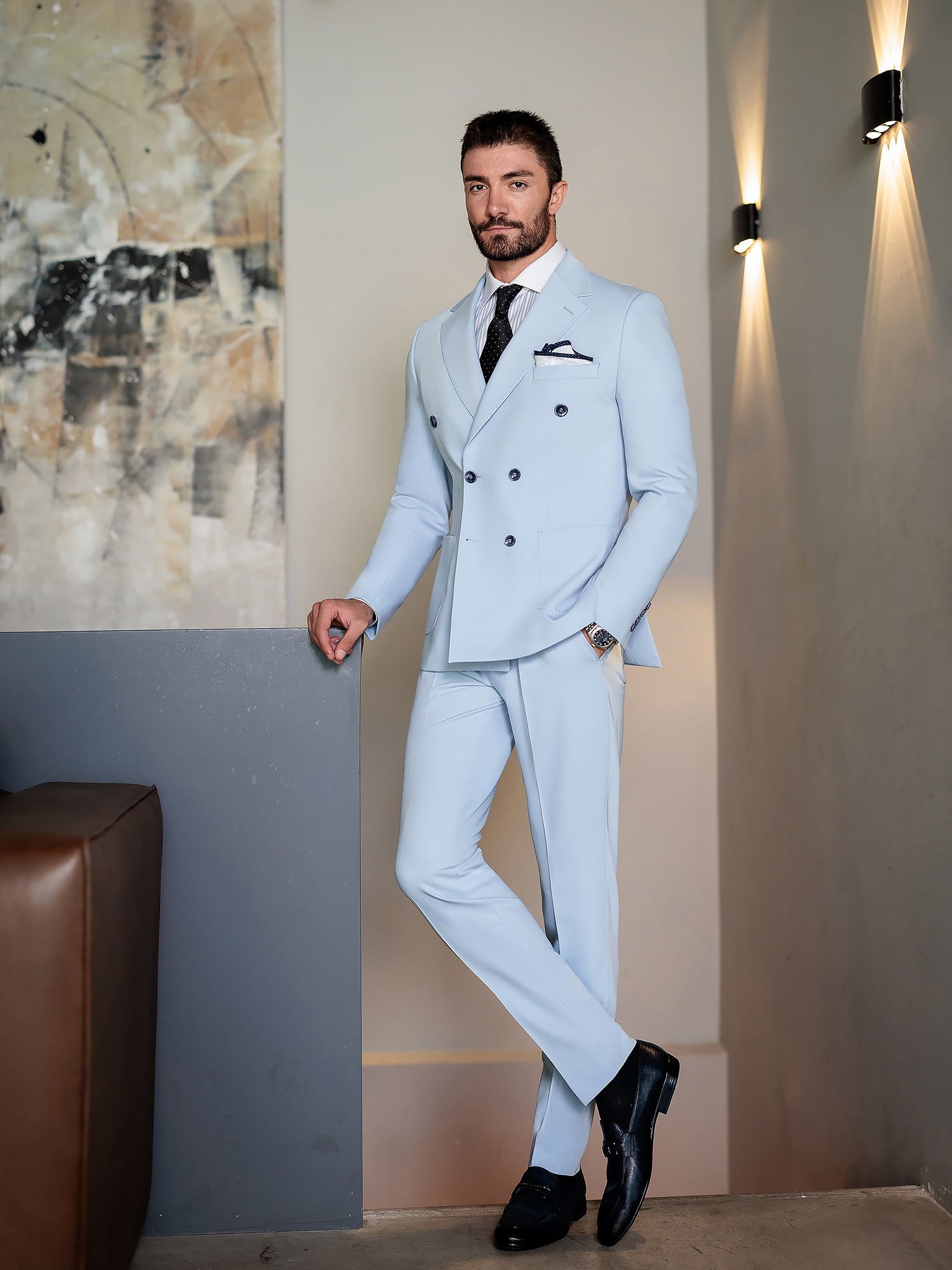 Men wearing a sky-blue double-breasted slim-fit suit with a white shirt and black tie, styled in a modern indoor setting.