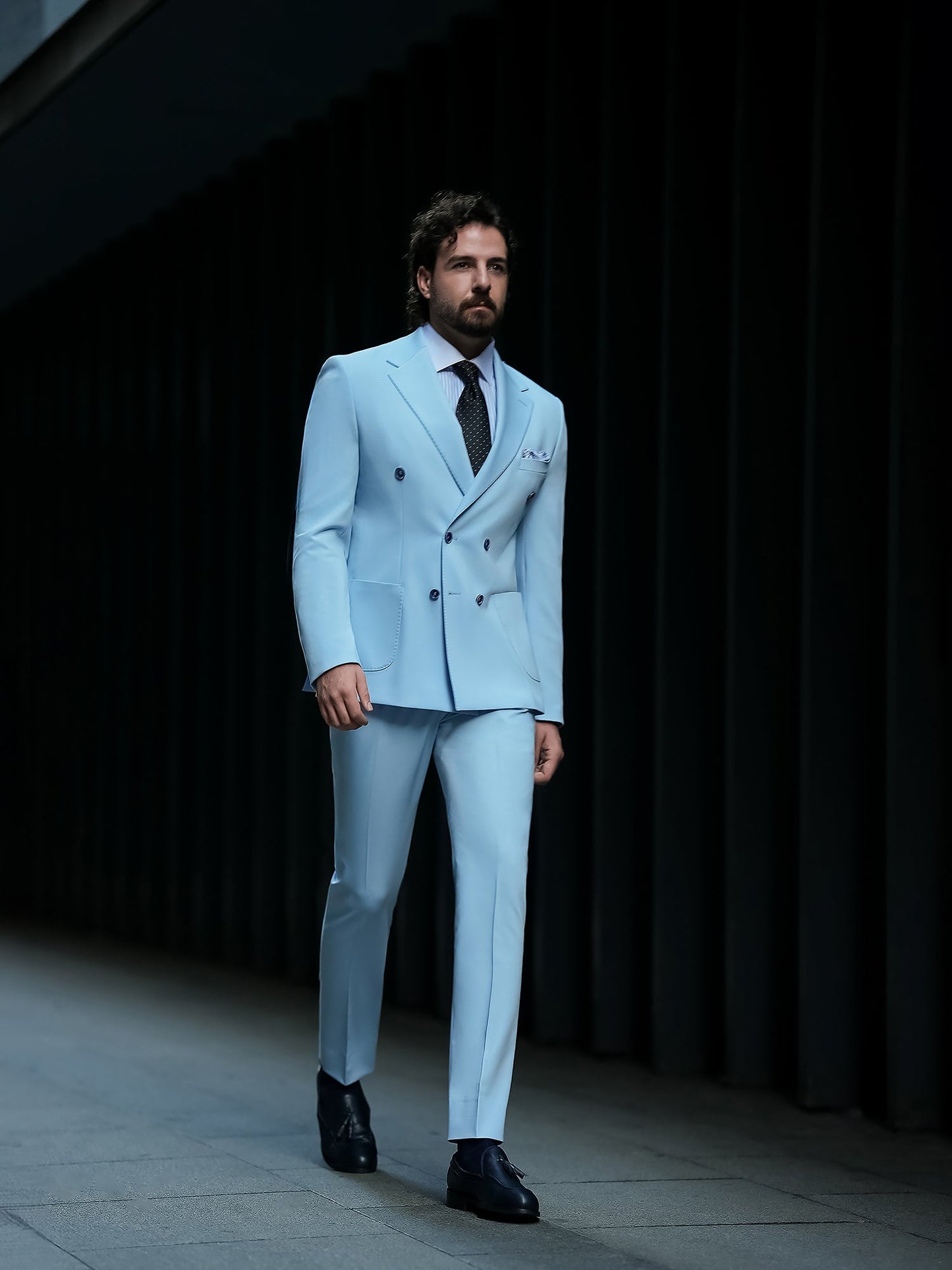 Men wearing a sky-blue double-breasted slim-fit suit with a white shirt and black tie, styled in a modern indoor setting.