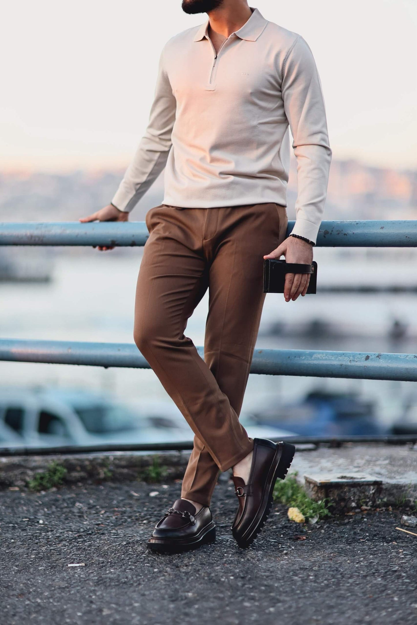 Men’s beige quarter-zip long sleeve polo shirt worn with camel trousers in an outdoor setting