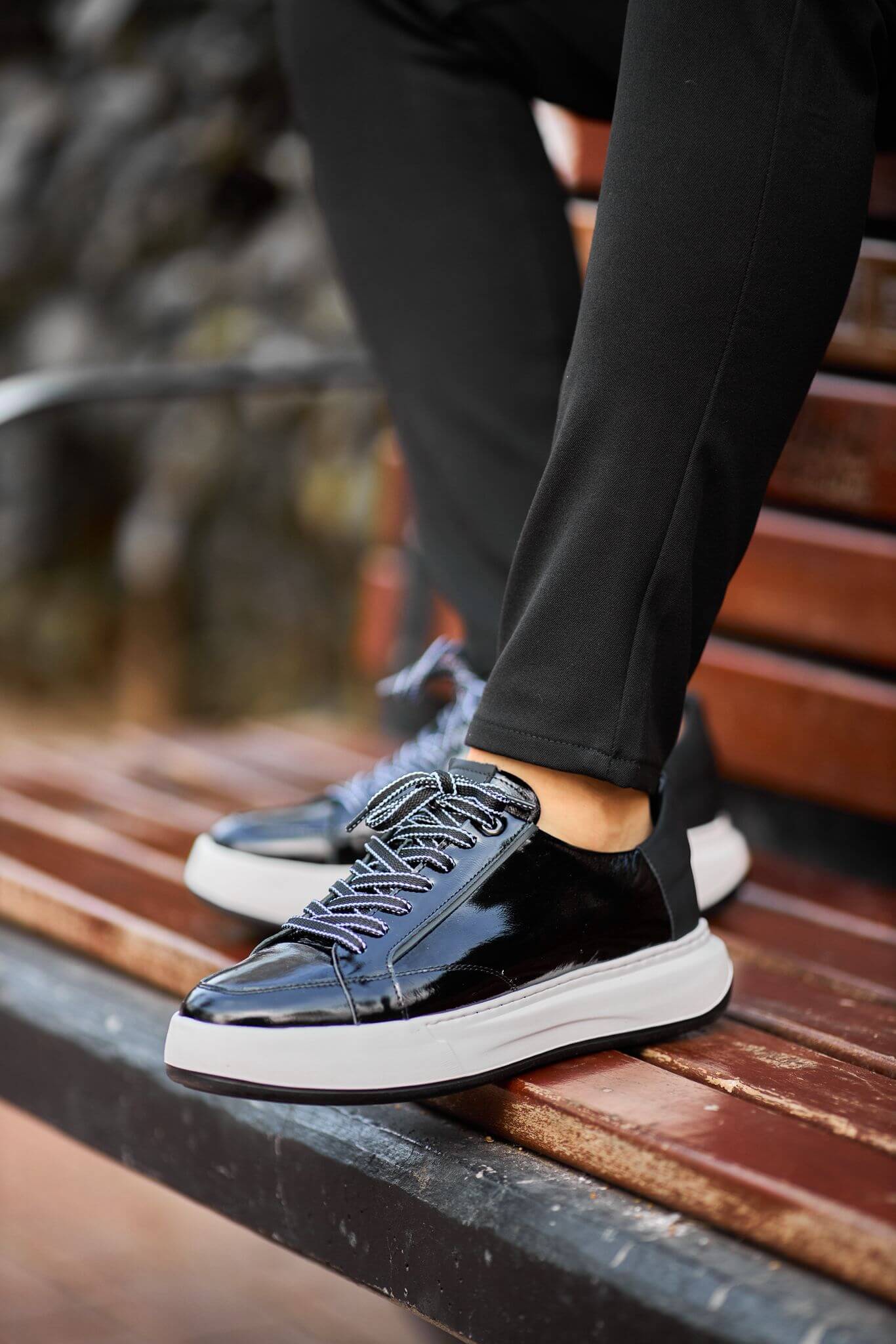 Black patent leather platform sneakers worn with black pants, shown on brick steps.