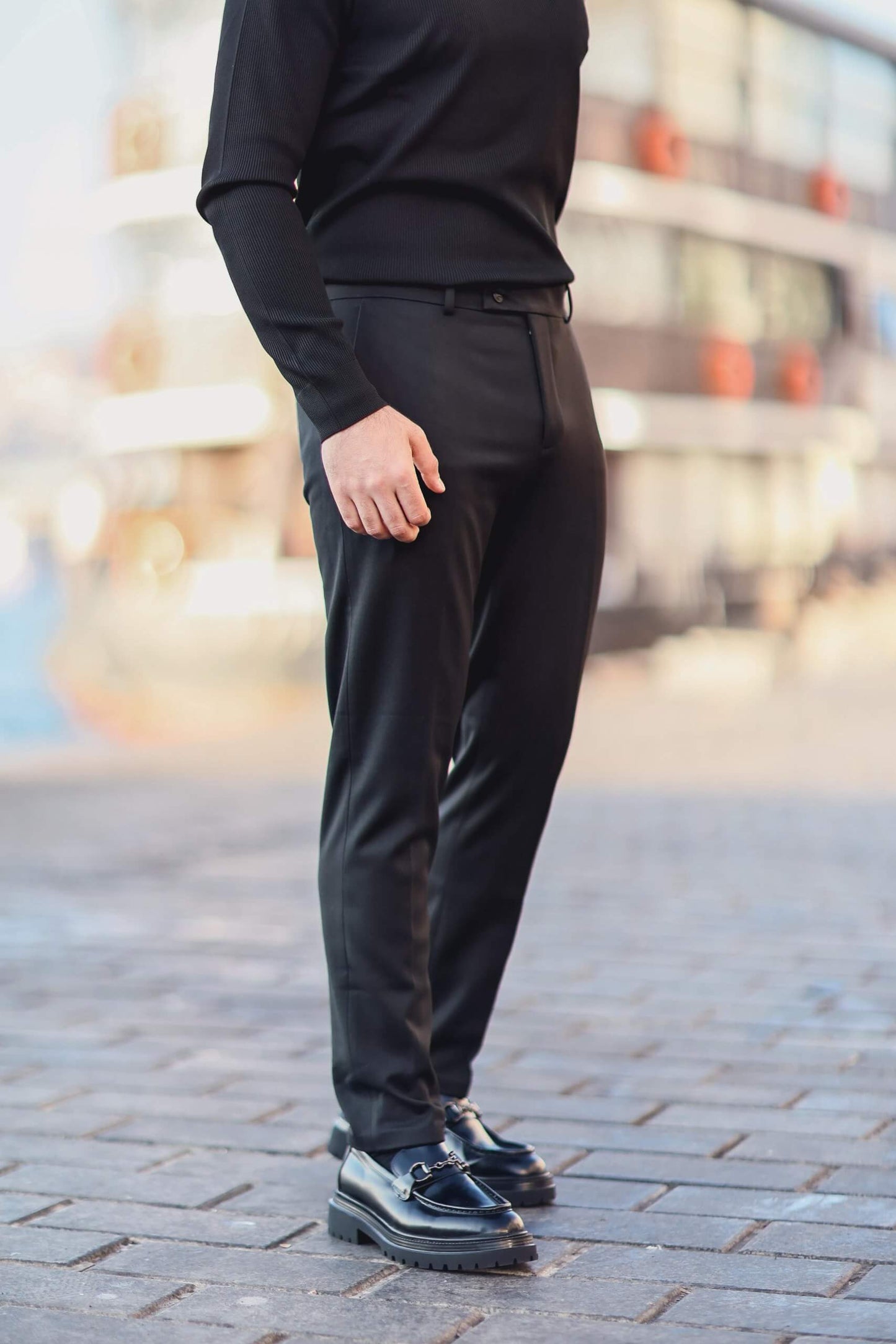 Man wearing black slim-fit tailored trousers with hands in pockets, styled with a black ribbed top.