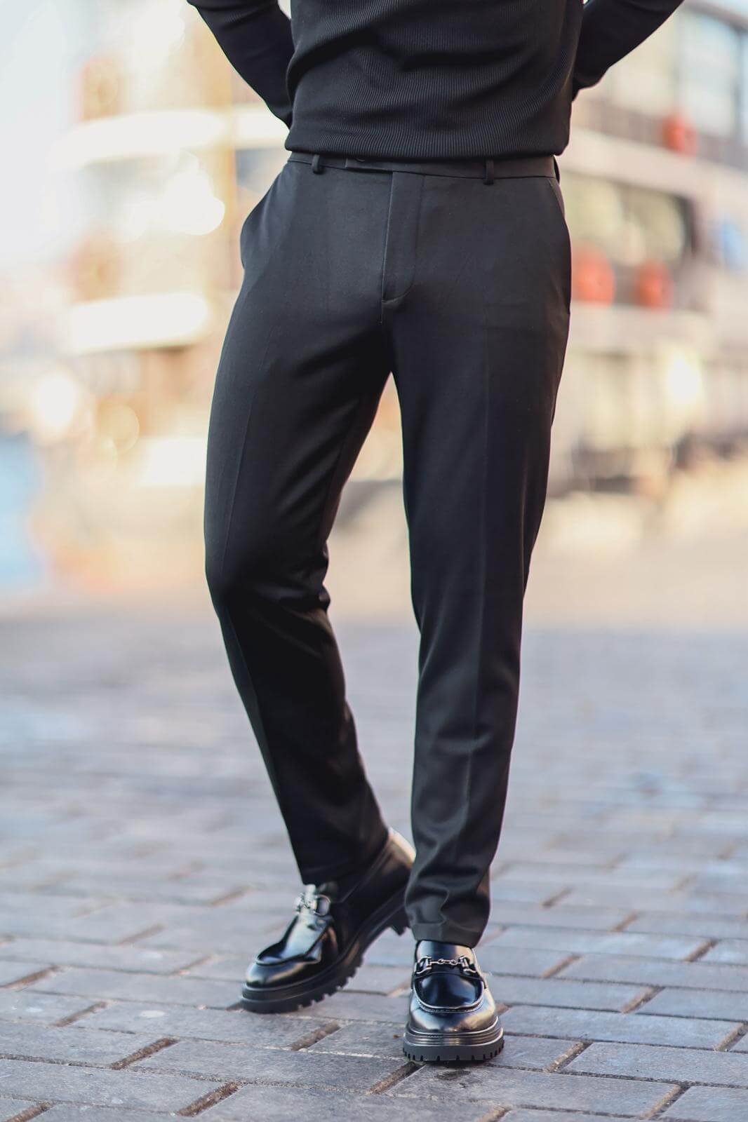 Man wearing black slim-fit tailored trousers with hands in pockets, styled with a black ribbed top.