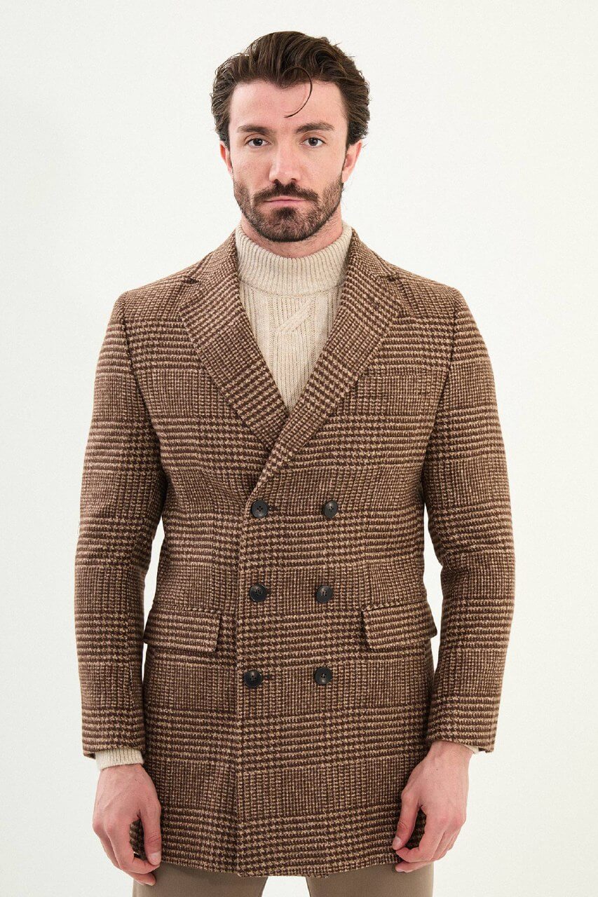 Men’s brown double-breasted herringbone wool-blend longline overcoat with extra-wide peak lapels, deep overlap front, and styled with a cream turtleneck.