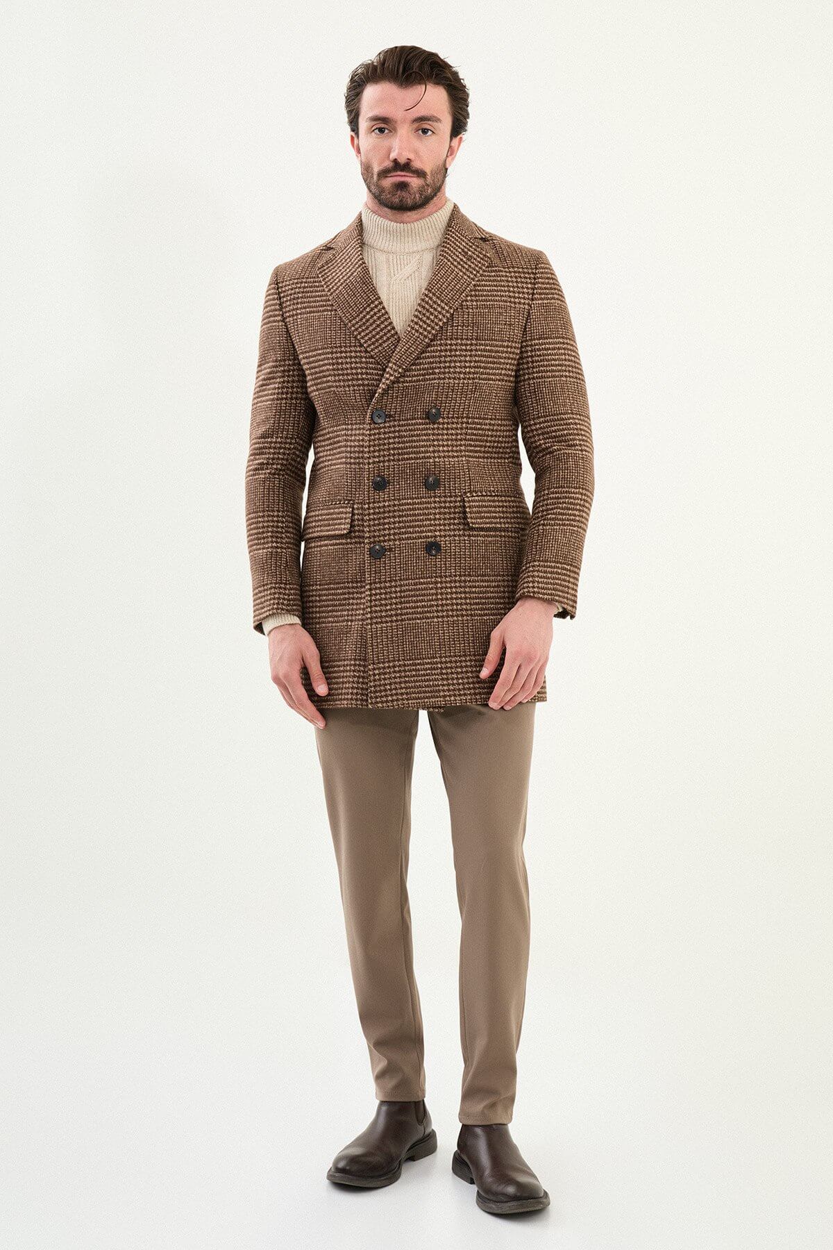 Men’s brown double-breasted herringbone wool-blend longline overcoat with extra-wide peak lapels, deep overlap front, and styled with a cream turtleneck.