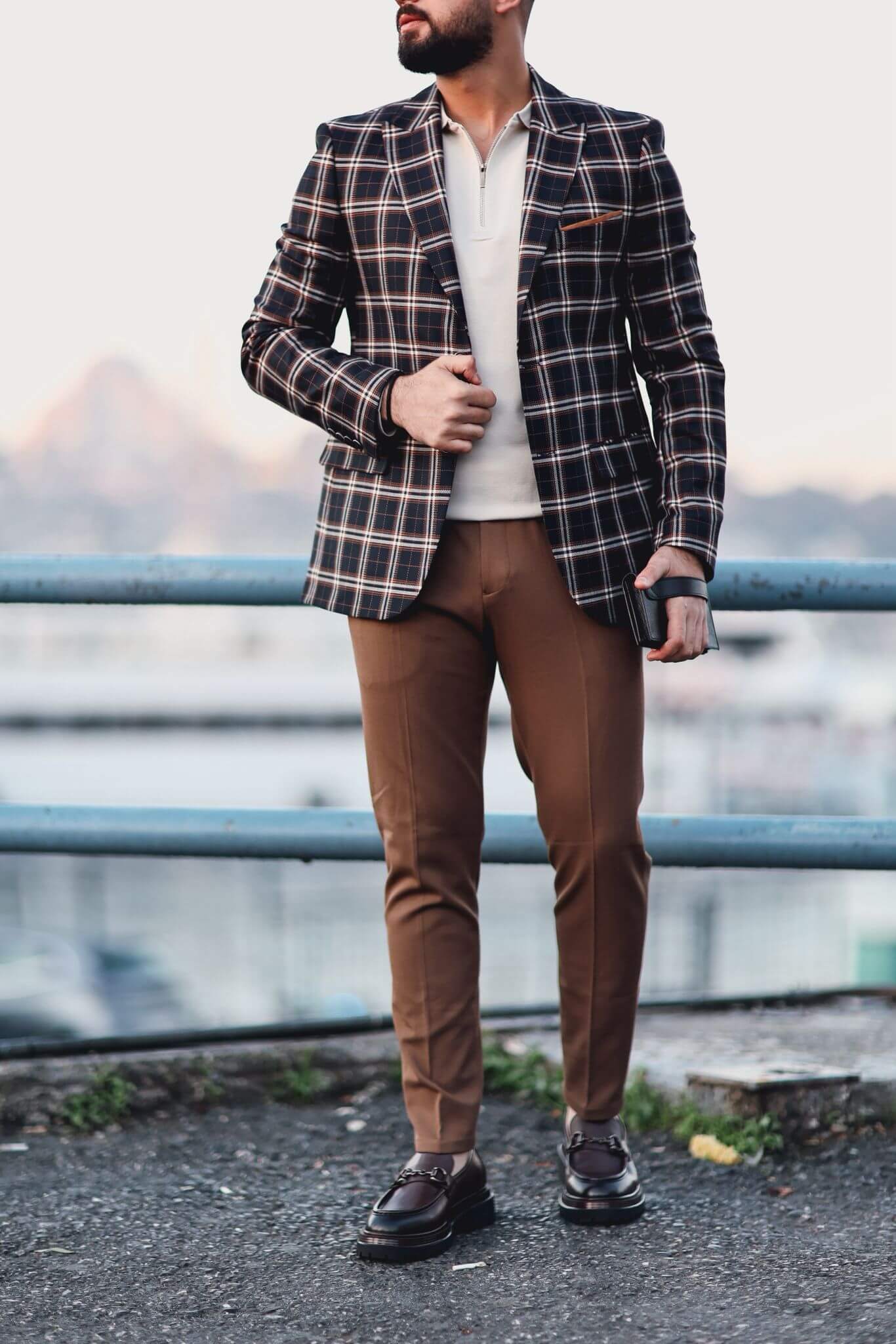 Man wearing camel slim-fit trousers styled with a checked blazer and loafers, photographed outdoors.